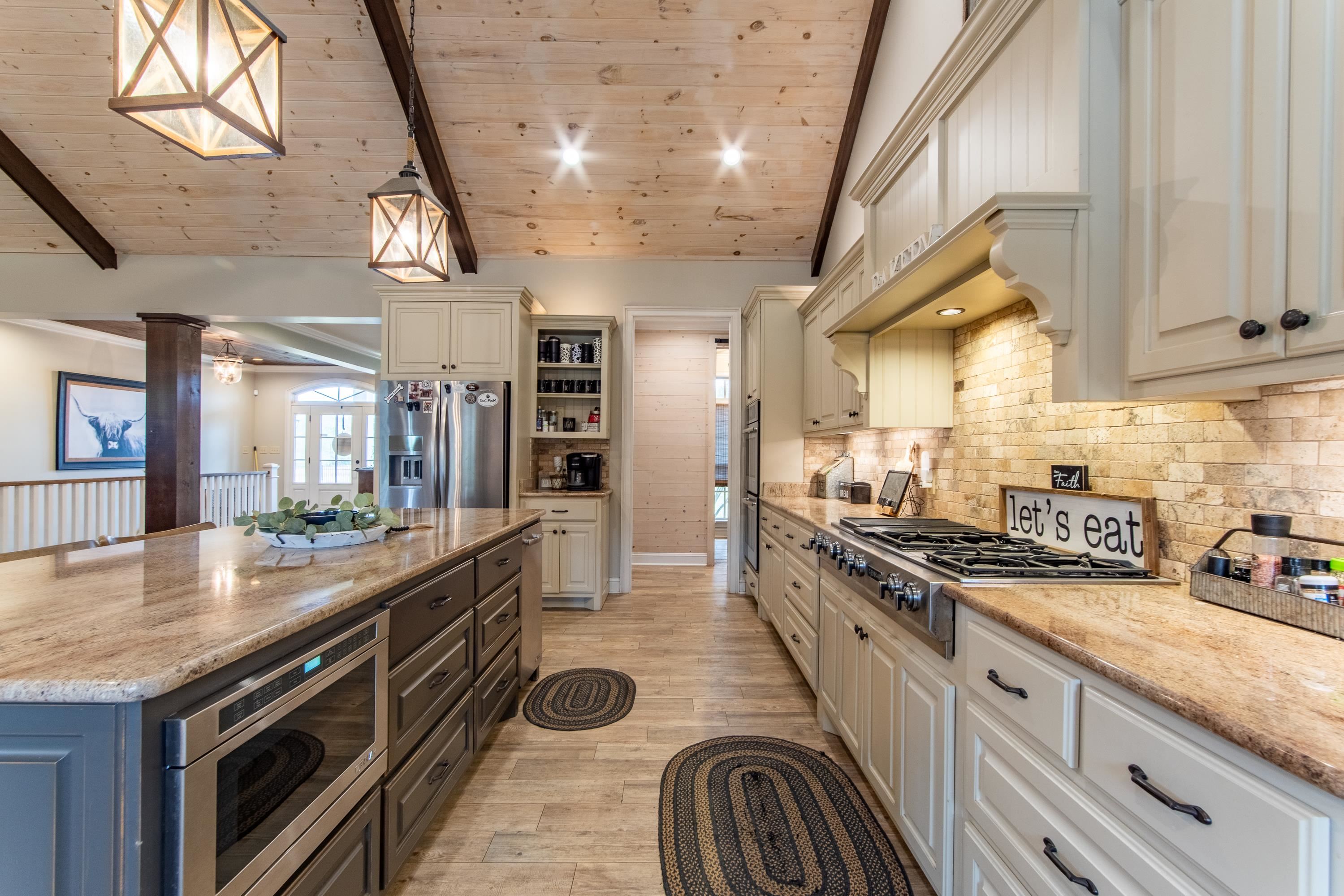 Kitchen featuring hanging light fixtures, light stone counters, a kitchen island, decorative columns, and stainless steel appliances