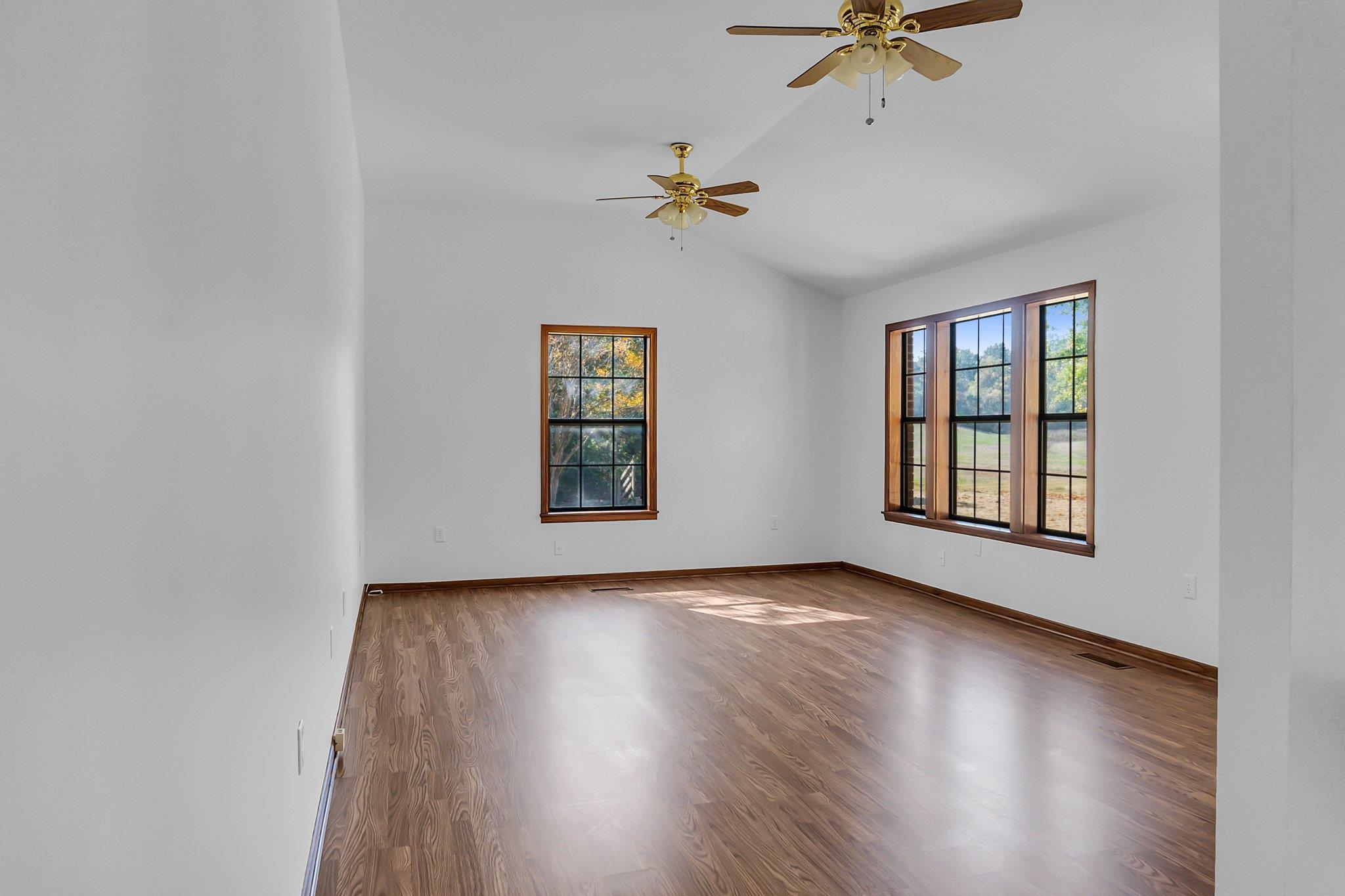 Empty room with ceiling fan, laminate wood-style flooring, and lofted ceiling