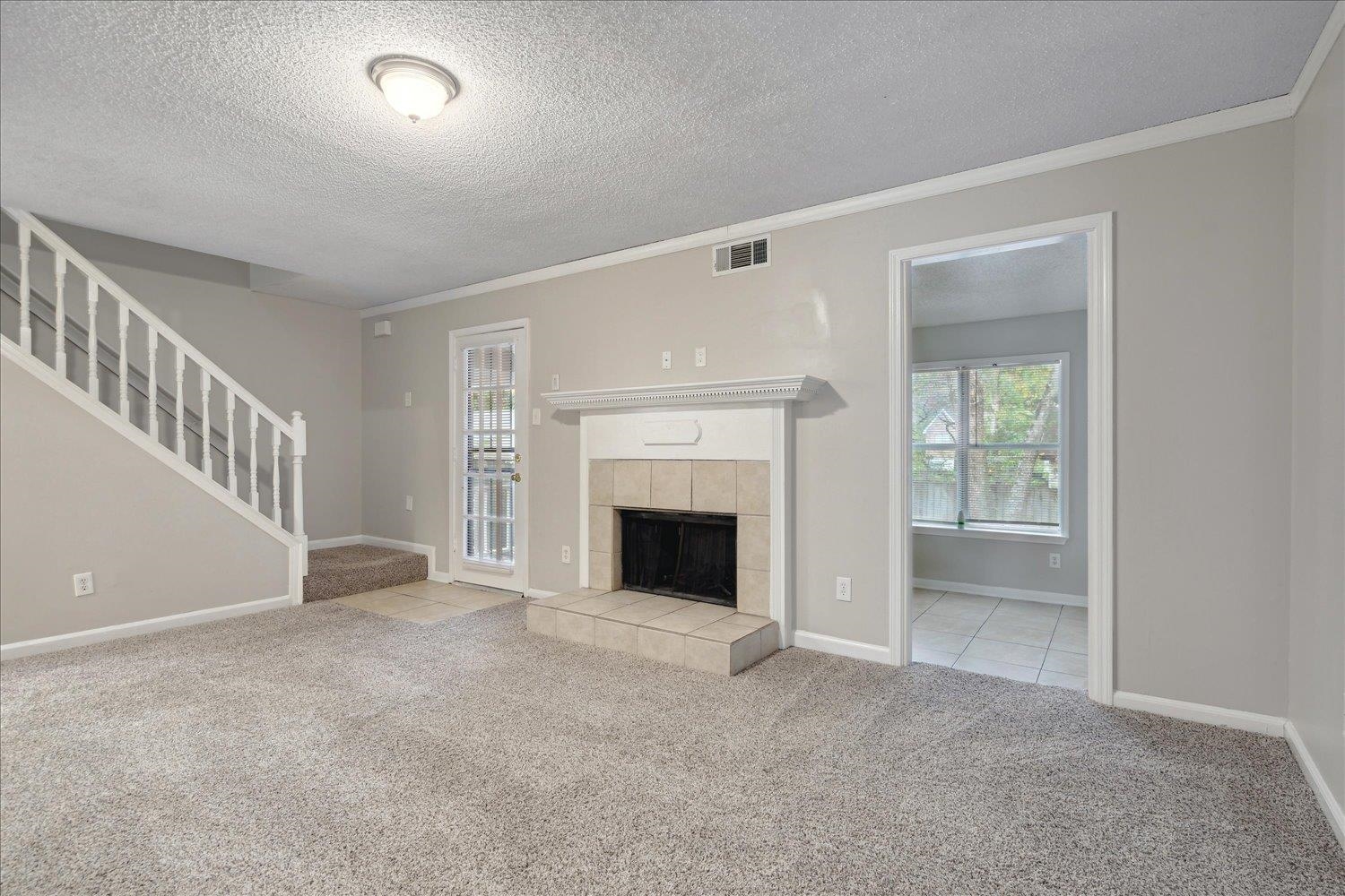 Unfurnished living room featuring ornamental molding, light colored carpet, a tile fireplace, and a textured ceiling