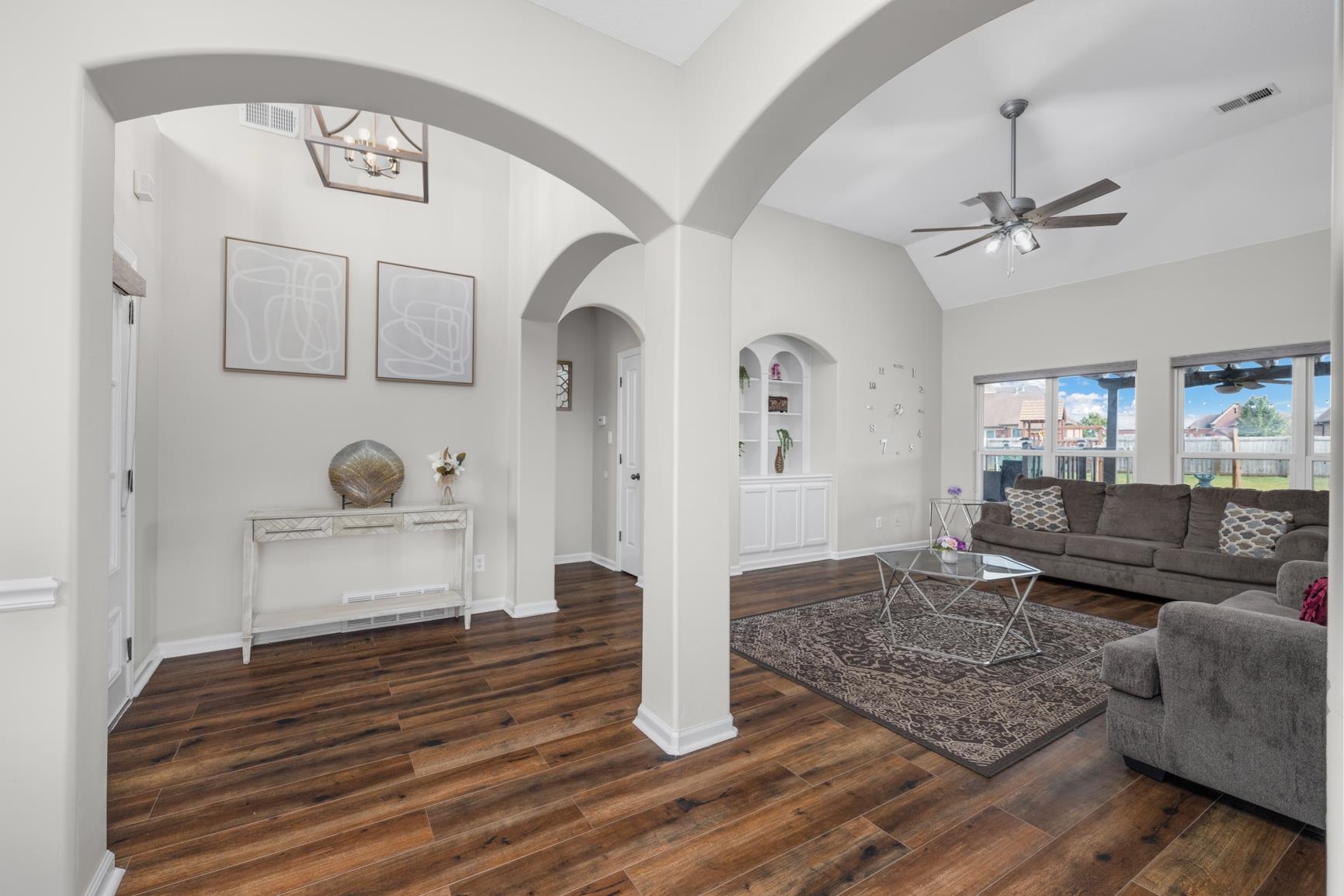 Living room featuring built in shelves, dark wood-type flooring, ceiling fan with notable chandelier, and vaulted ceiling