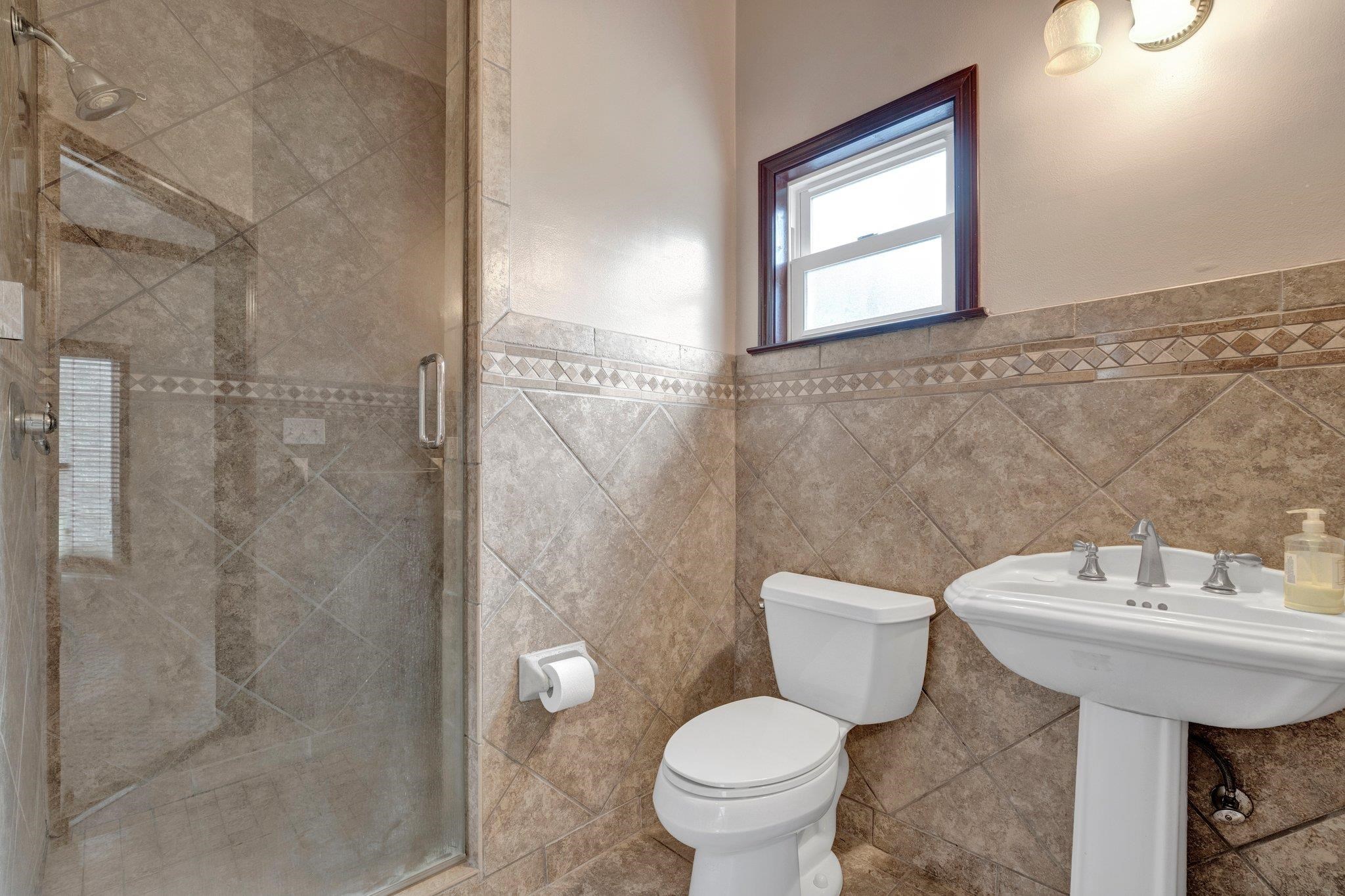 Bathroom featuring toilet, walk in shower, and tile walls