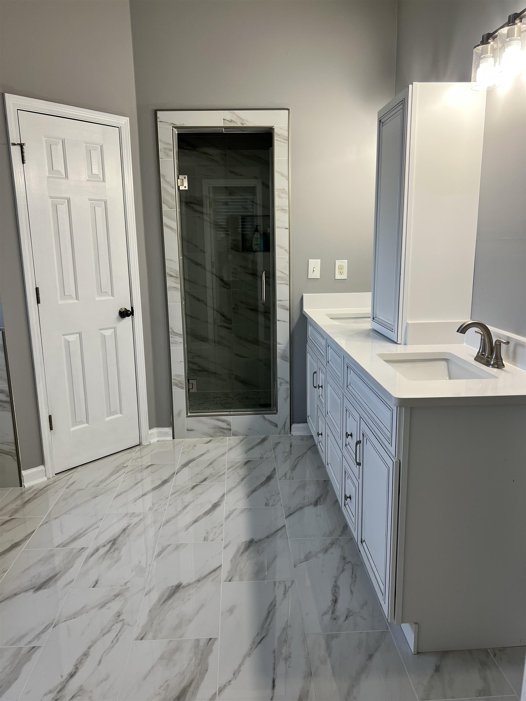 Bathroom featuring a shower with shower door, tile patterned flooring, and dual bowl vanity