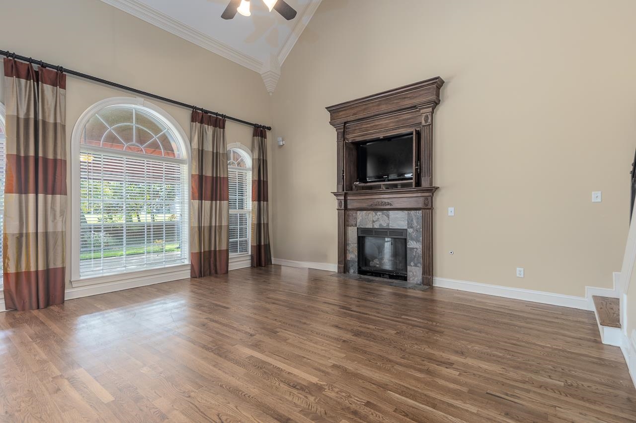 Unfurnished living room with crown molding, hardwood / wood-style floors, a tiled fireplace, and high vaulted ceiling