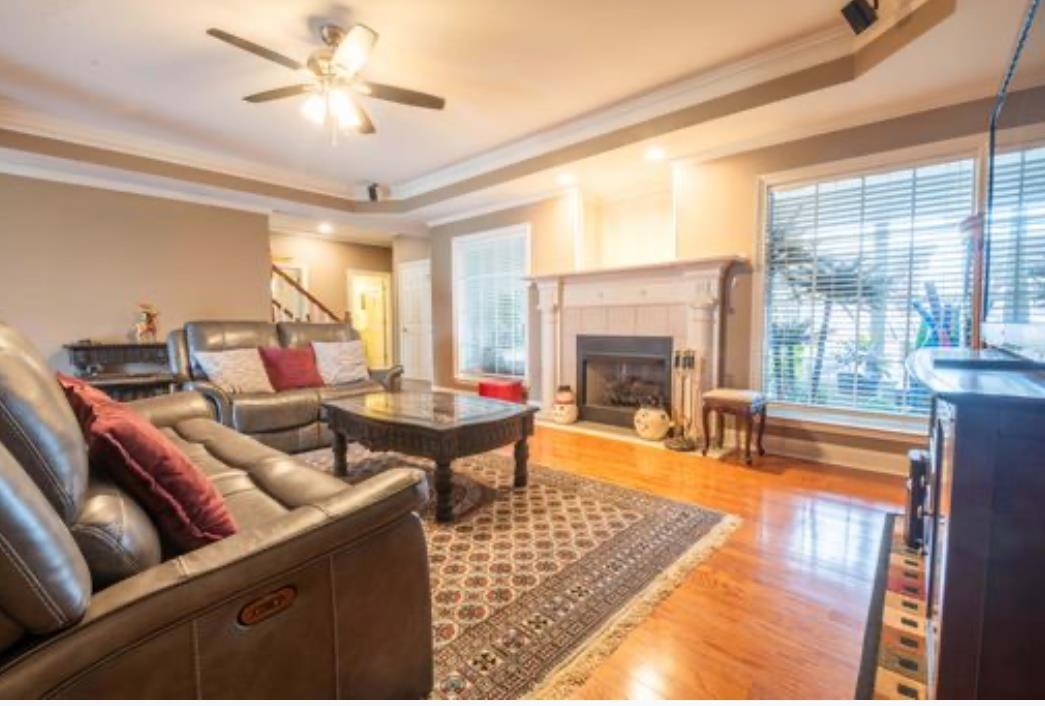 Living room with light hardwood / wood-style floors, a tile fireplace, ceiling fan, crown molding, and a raised ceiling