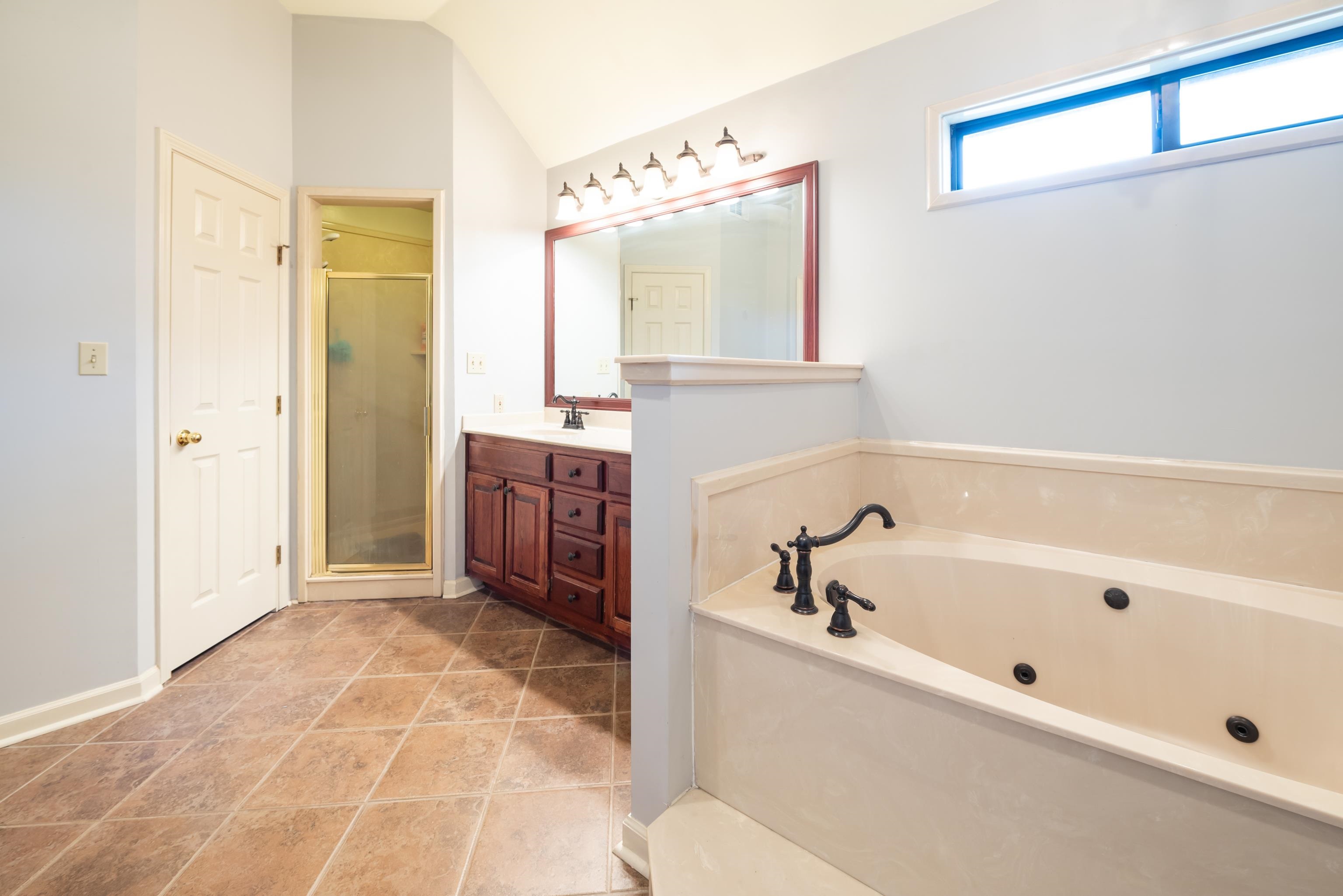 Bathroom with vanity, vaulted ceiling, tile patterned floors, and separate shower and tub