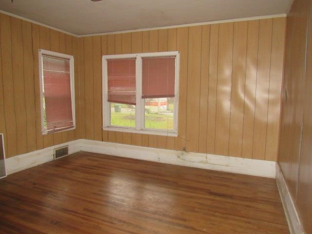 Unfurnished room featuring wood walls, dark wood-type flooring, and crown molding