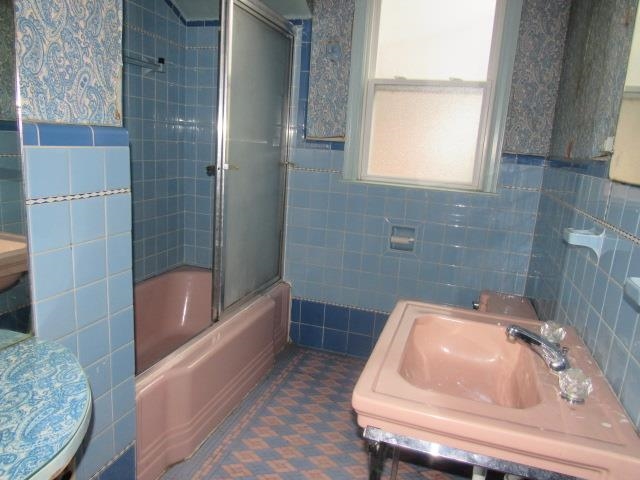 Full bathroom featuring toilet, vanity, tile walls, and enclosed tub / shower combo