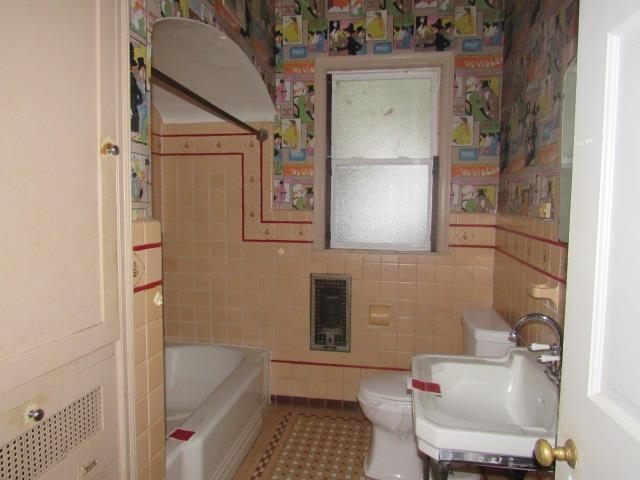 Bathroom with a tub, sink, tile patterned floors, toilet, and tile walls