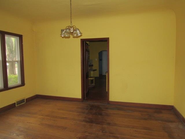 Empty room with a chandelier and dark hardwood / wood-style flooring