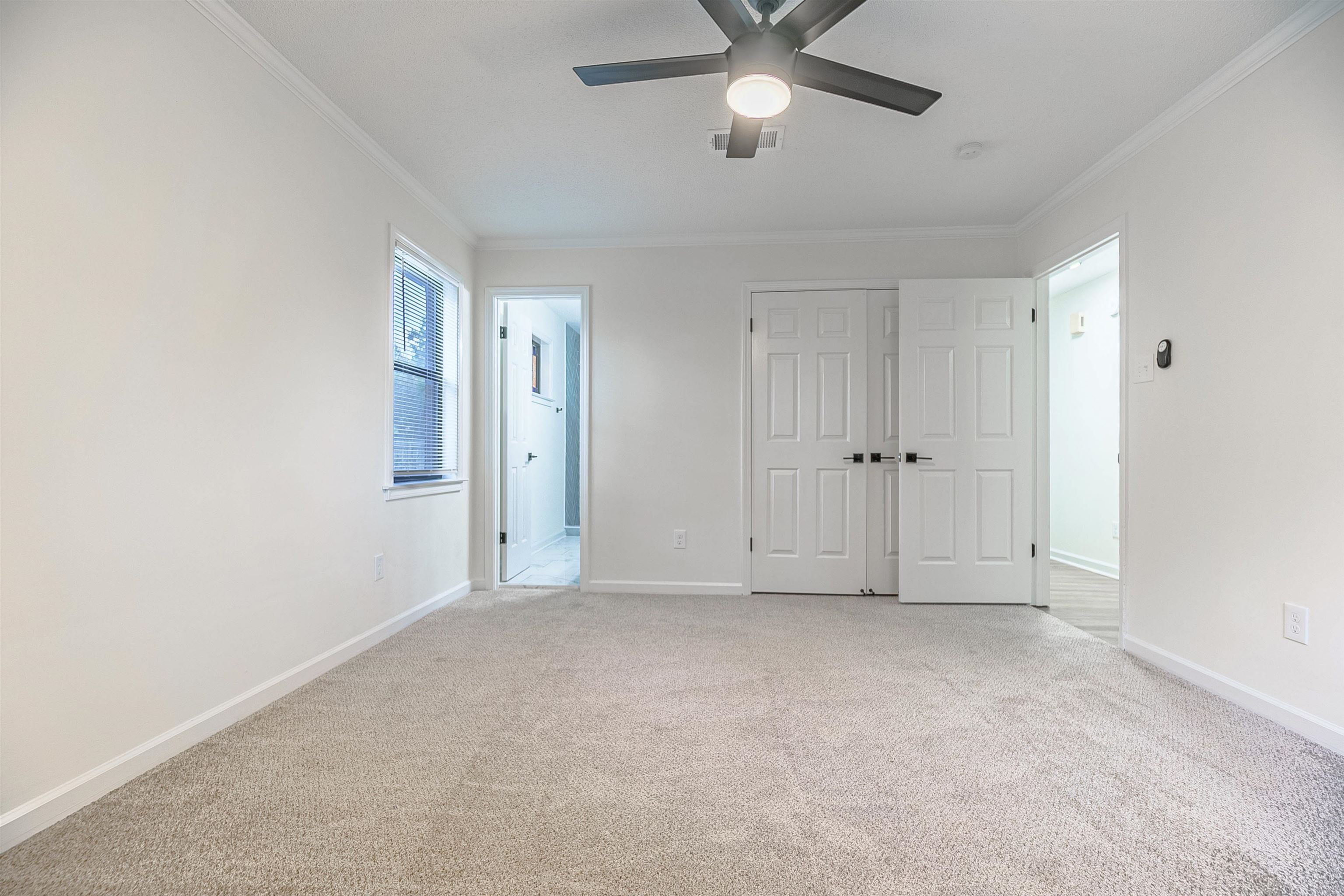 Unfurnished bedroom with ceiling fan, ensuite bath, light carpet, and crown molding