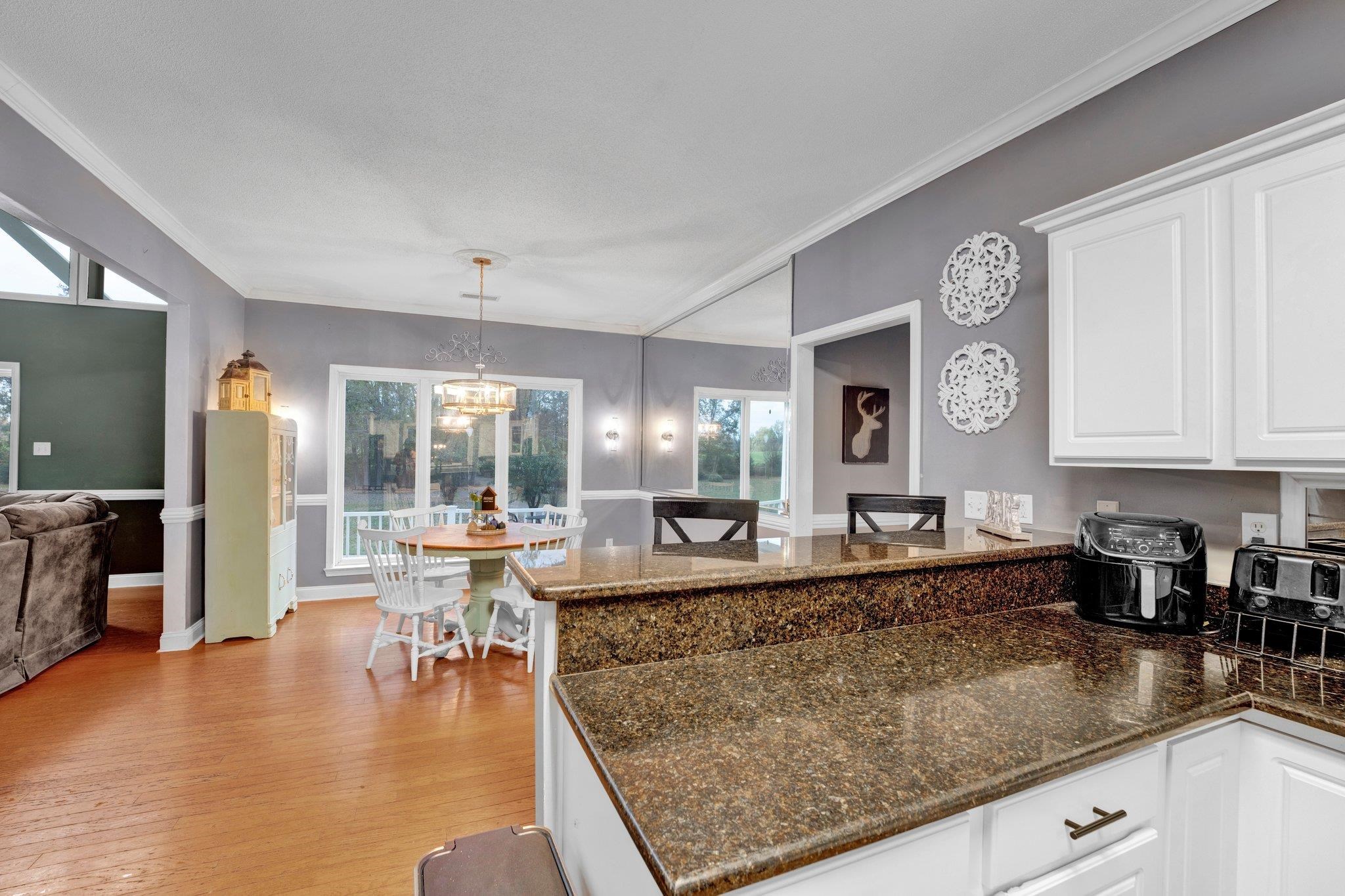 Kitchen featuring crown molding, white cabinetry, light wood-type flooring, pendant lighting, and an inviting chandelier