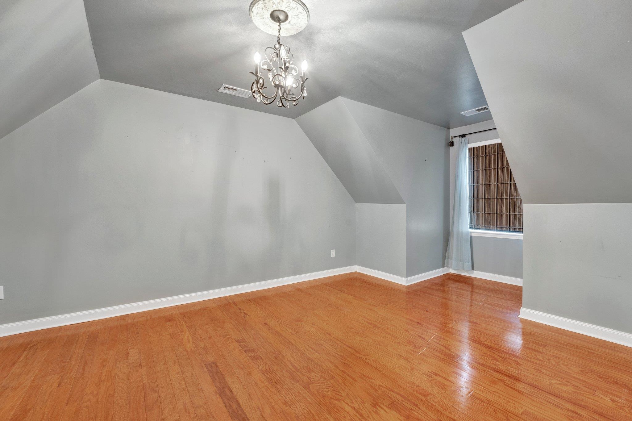 Bonus room featuring an inviting chandelier, hardwood / wood-style floors, and vaulted ceiling