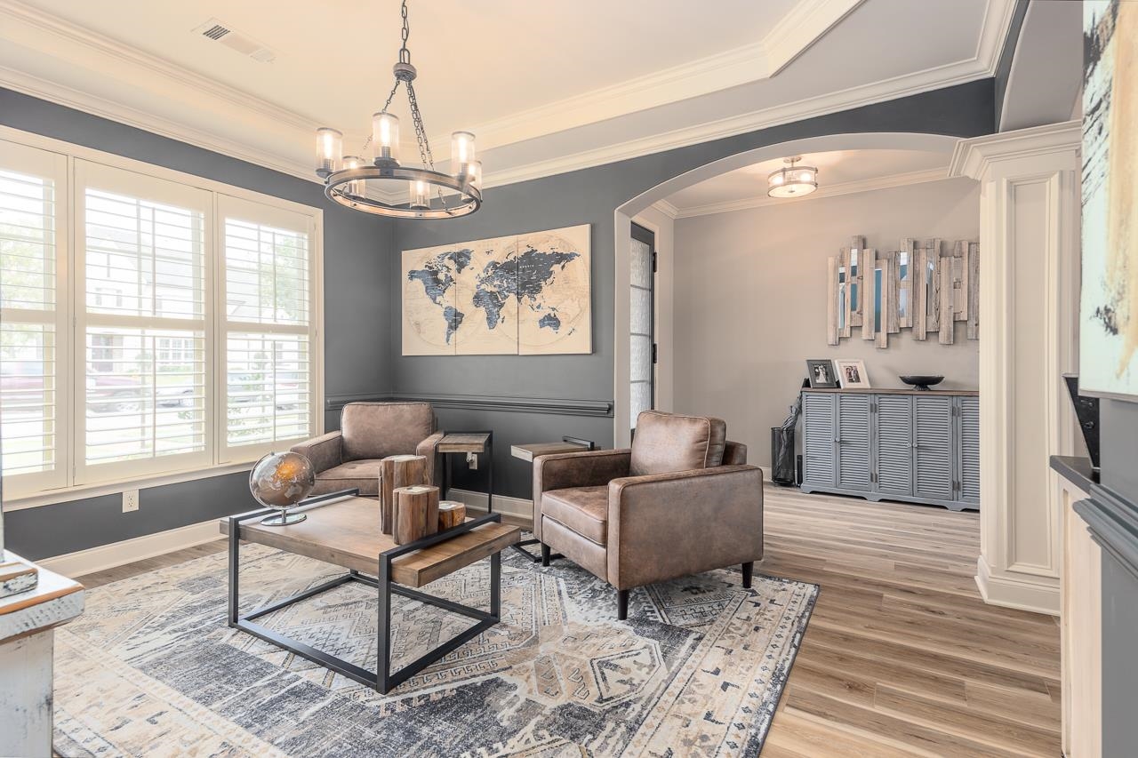 Dining room or sitting room with light wood-type flooring, a notable chandelier, and crown molding