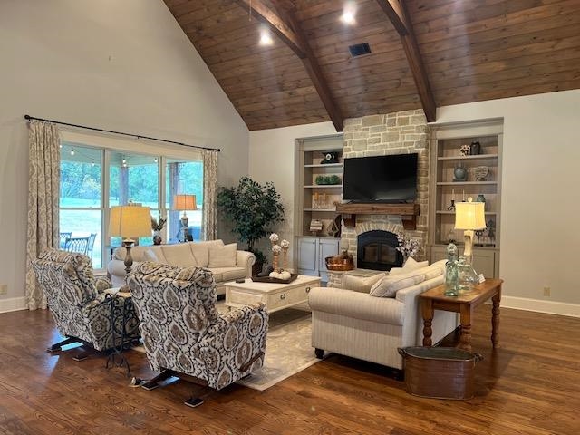 Living room featuring built in shelves, a stone fireplace, beam ceiling, wood ceiling, and dark wood-type flooring