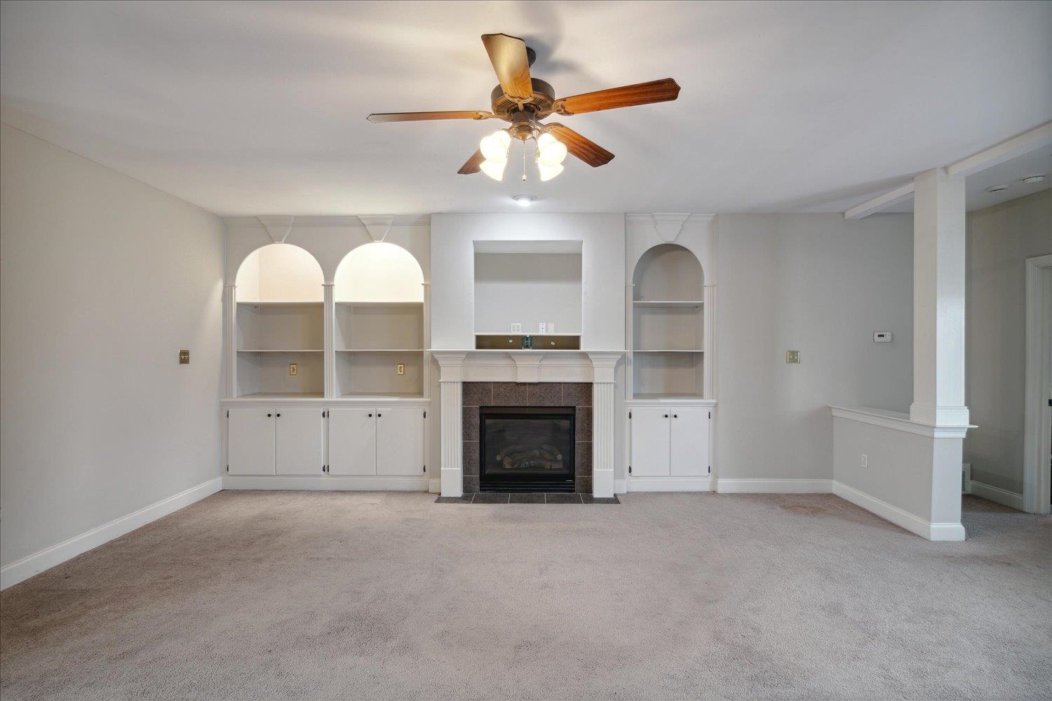 Unfurnished living room with light colored carpet, ceiling fan, and a tile fireplace