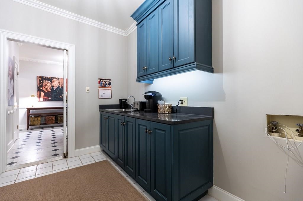 Bar with light tile patterned floors, blue cabinetry, sink, and crown molding