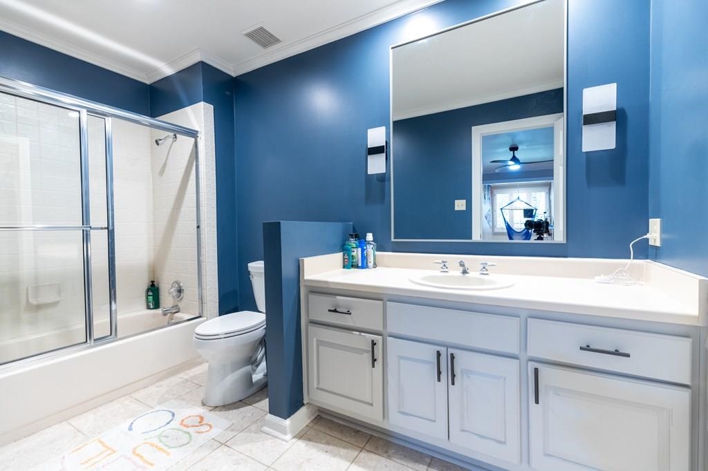 Full bathroom featuring ornamental molding, vanity, bath / shower combo with glass door, tile patterned floors, and toilet