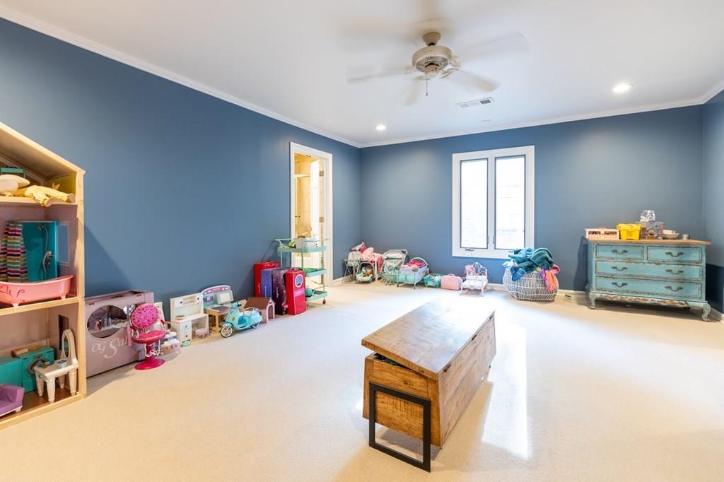 Recreation room with ceiling fan, crown molding, and carpet floors