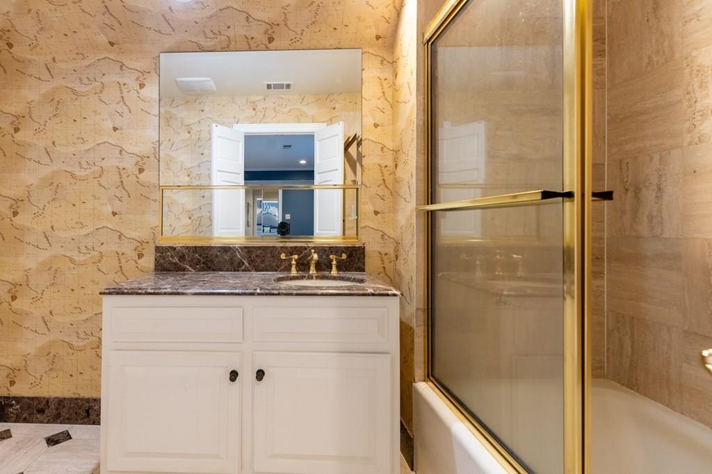 Bathroom with bath / shower combo with glass door and vanity
