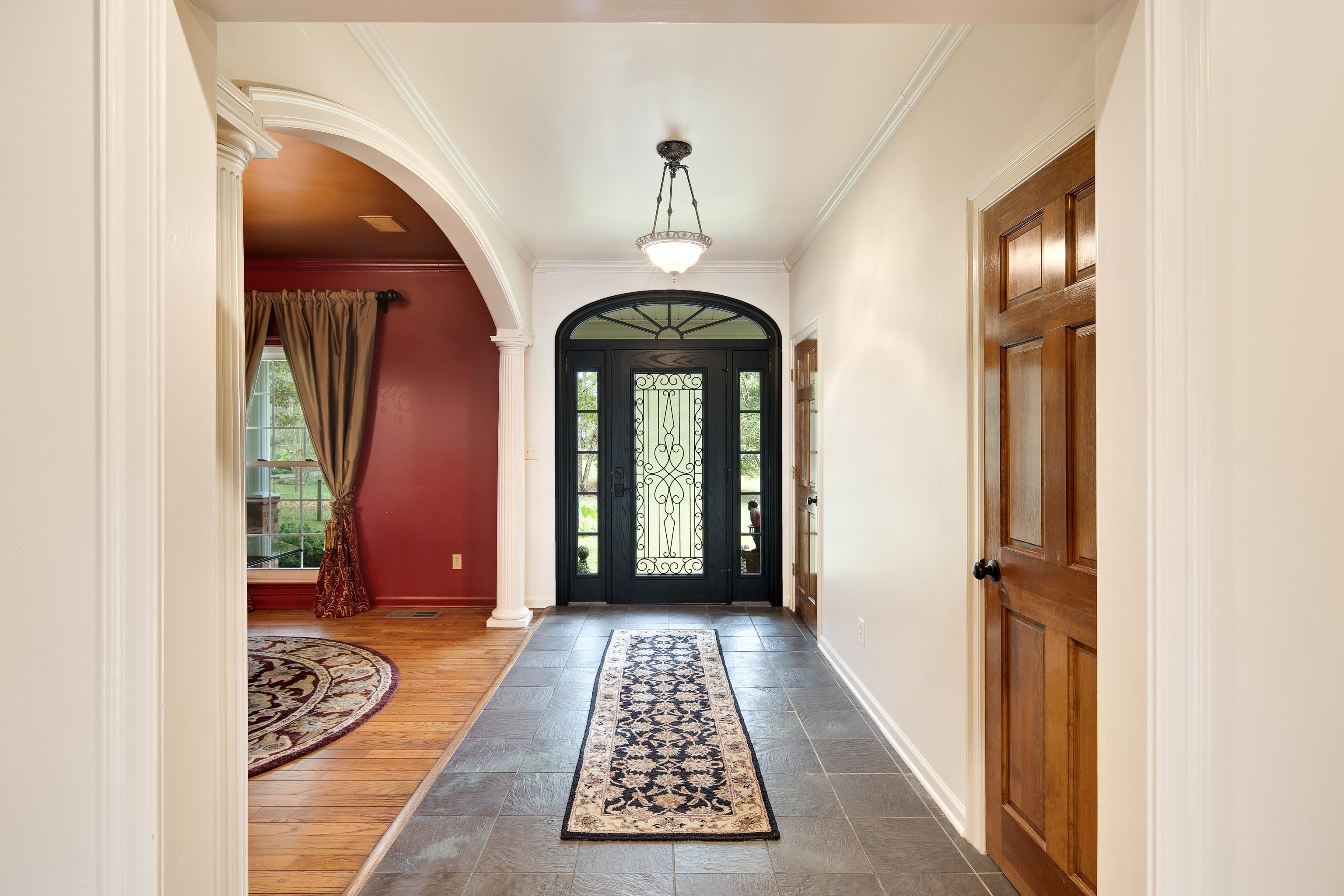 Foyer featuring dark wood-type flooring, crown molding, and decorative columns