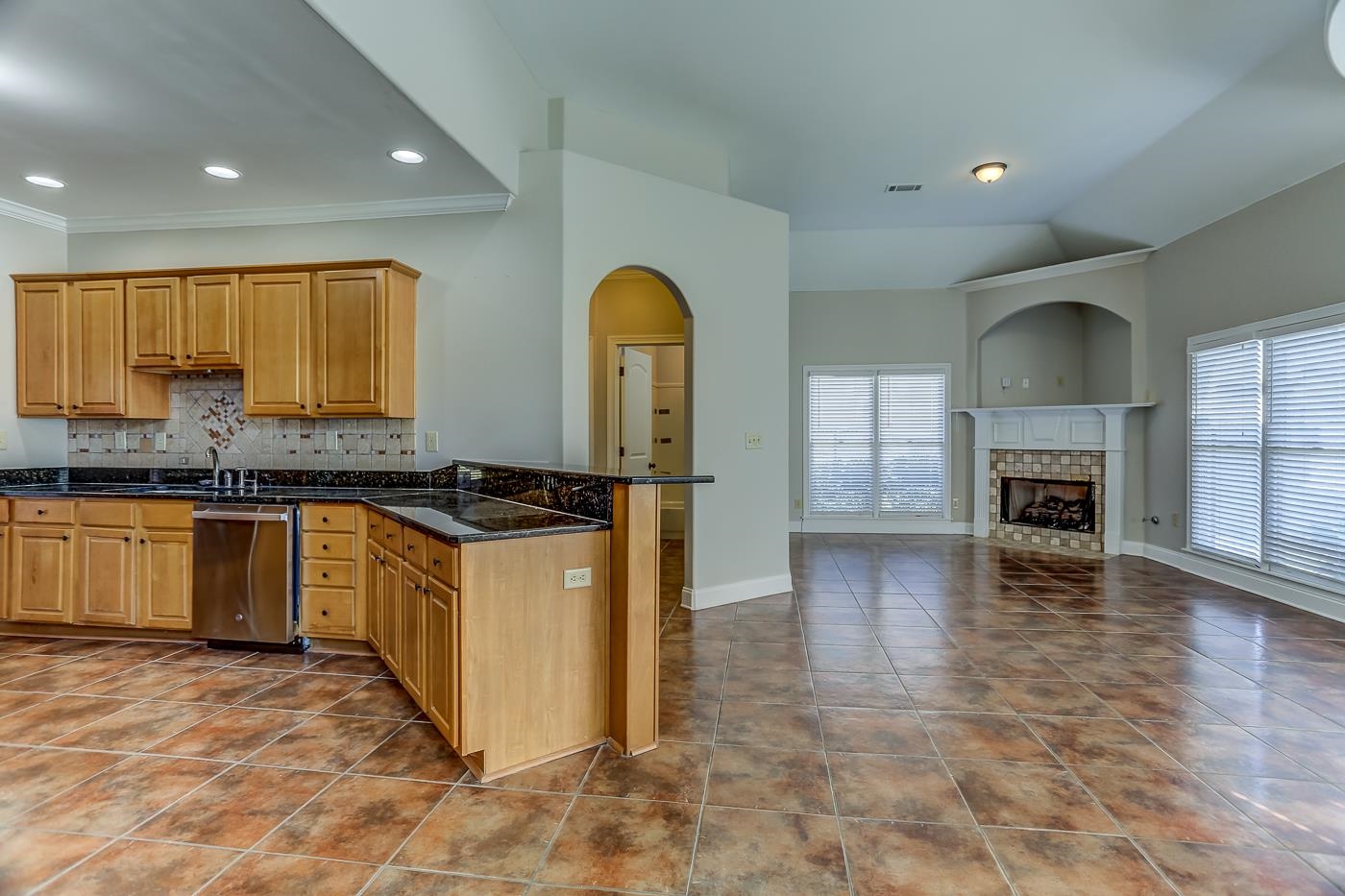 Kitchen featuring a tiled fireplace, kitchen peninsula, tasteful backsplash, dark stone countertops, and stainless steel dishwasher