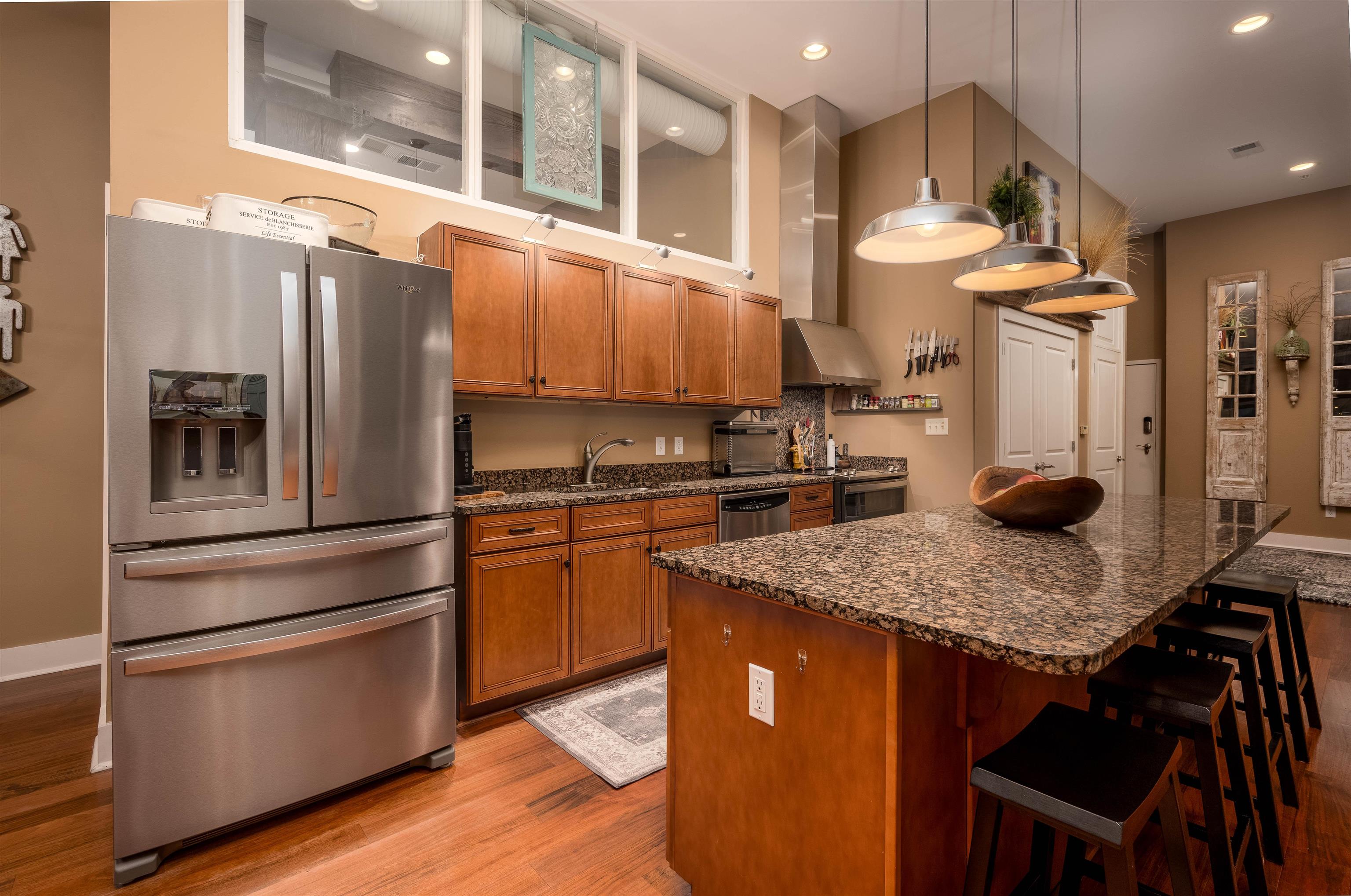 Kitchen with dark stone counters, appliances with stainless steel finishes, hanging light fixtures, a kitchen breakfast bar, and light hardwood / wood-style floors