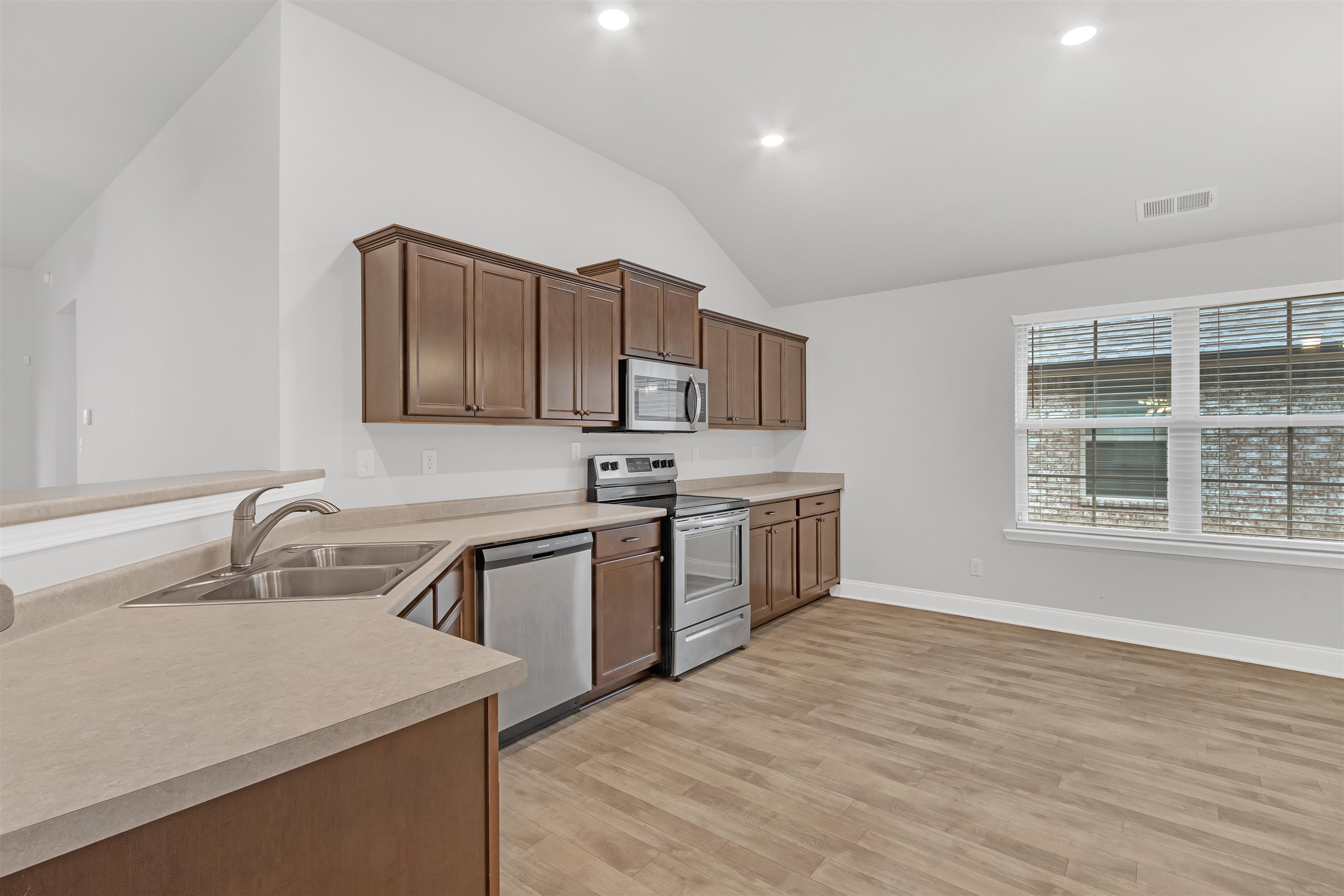 Kitchen with stainless steel appliances, lofted ceiling, kitchen peninsula, sink, and light wood-type flooring