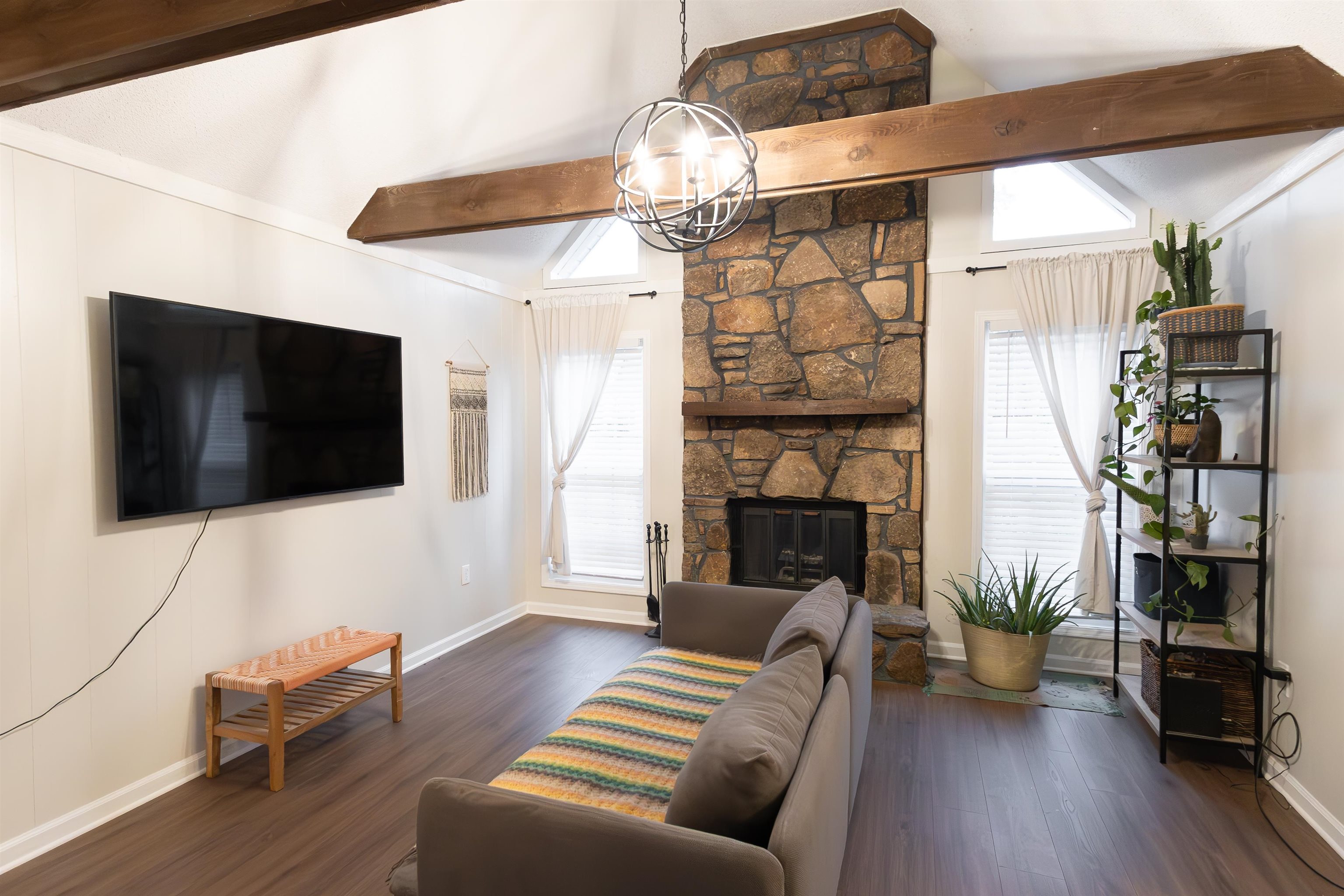 Living room with a stone fireplace, vaulted ceiling with beams, dark hardwood / wood-style floors, and a chandelier