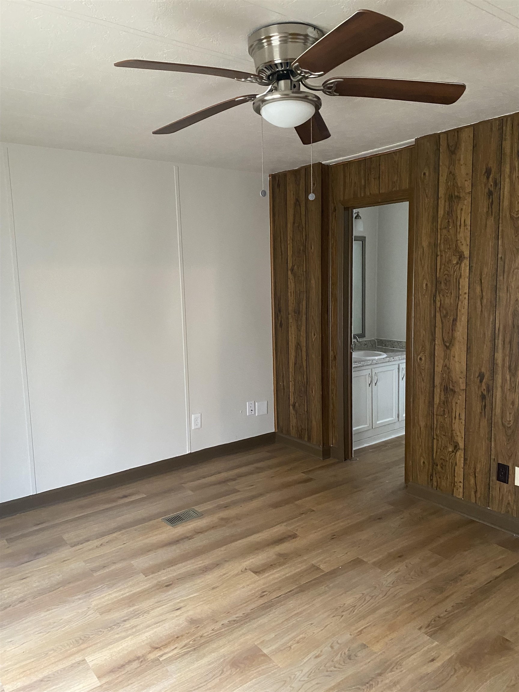 Empty room with light hardwood / wood-style floors, ceiling fan, and wooden walls