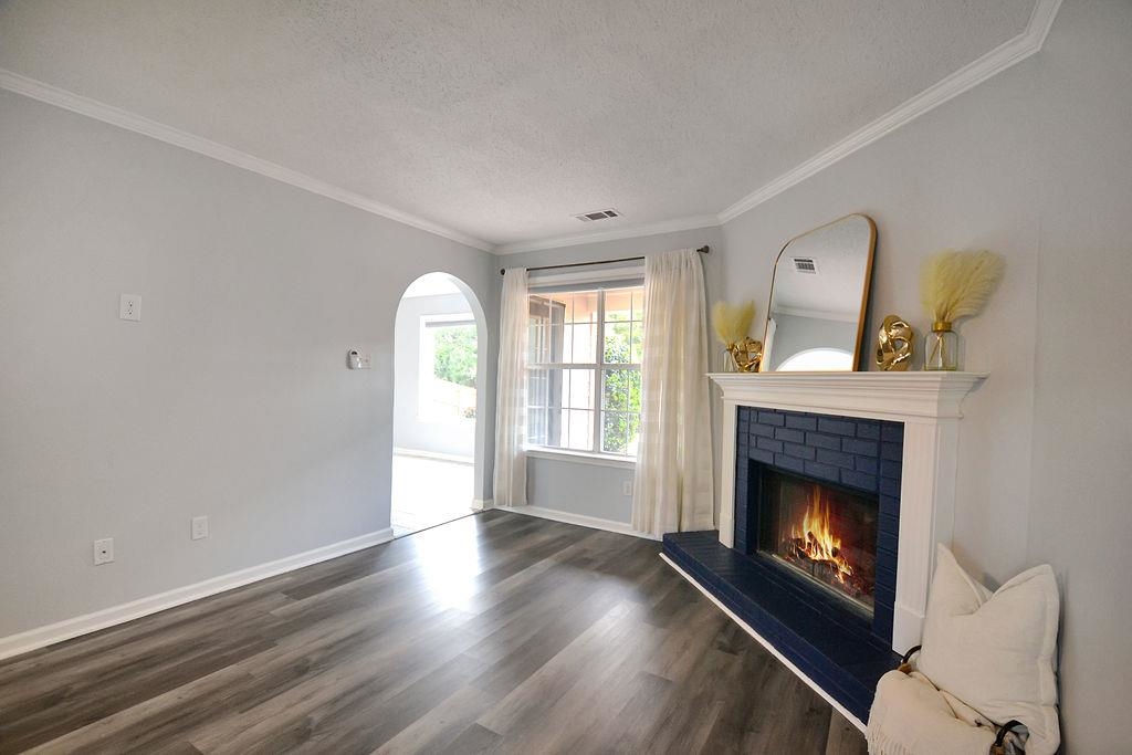 Unfurnished living room with ornamental molding, a textured ceiling, dark hardwood / wood-style floors, and a brick fireplace