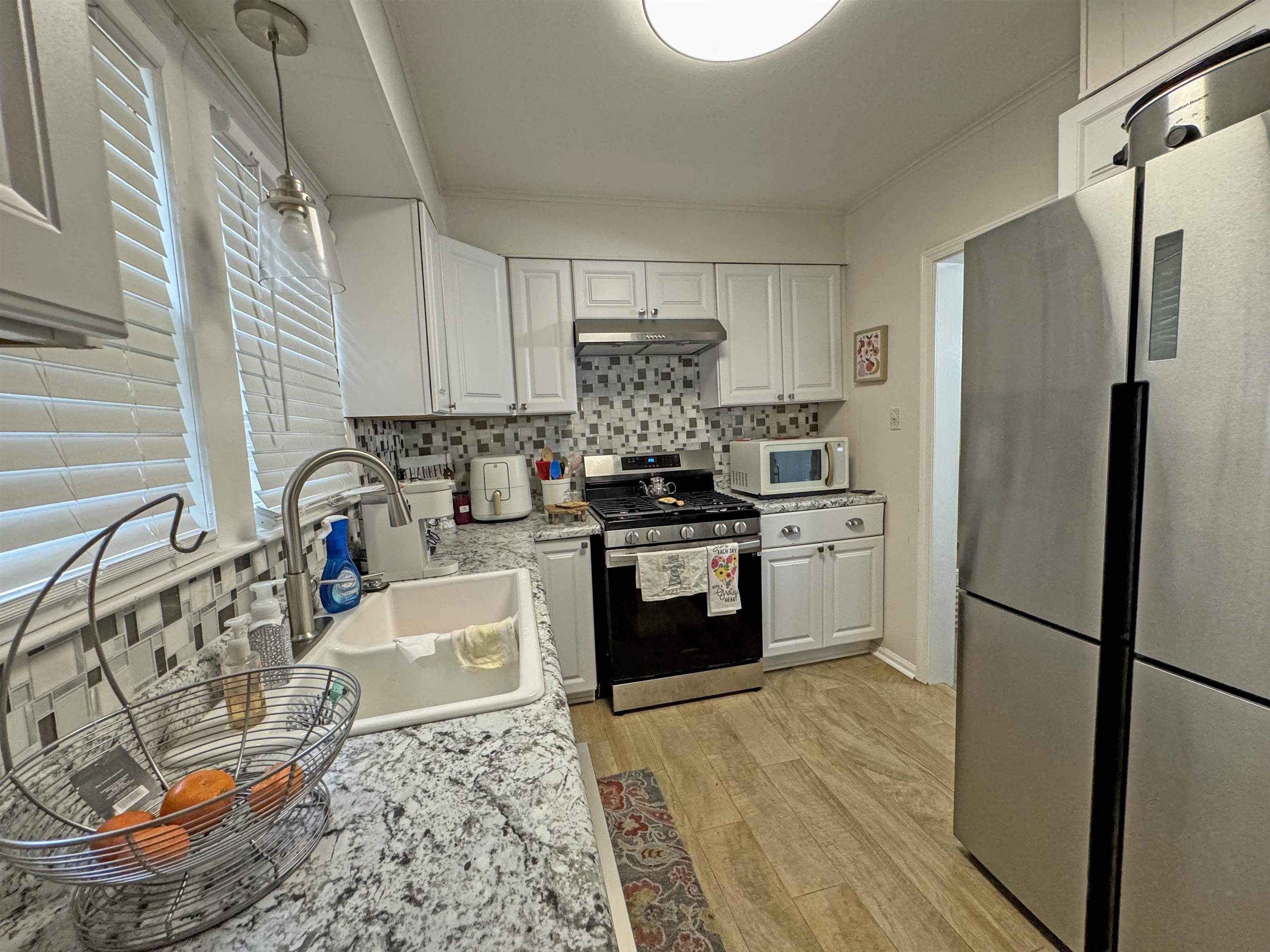 Kitchen featuring light wood-type flooring, appliances with stainless steel finishes, backsplash, and white cabinets