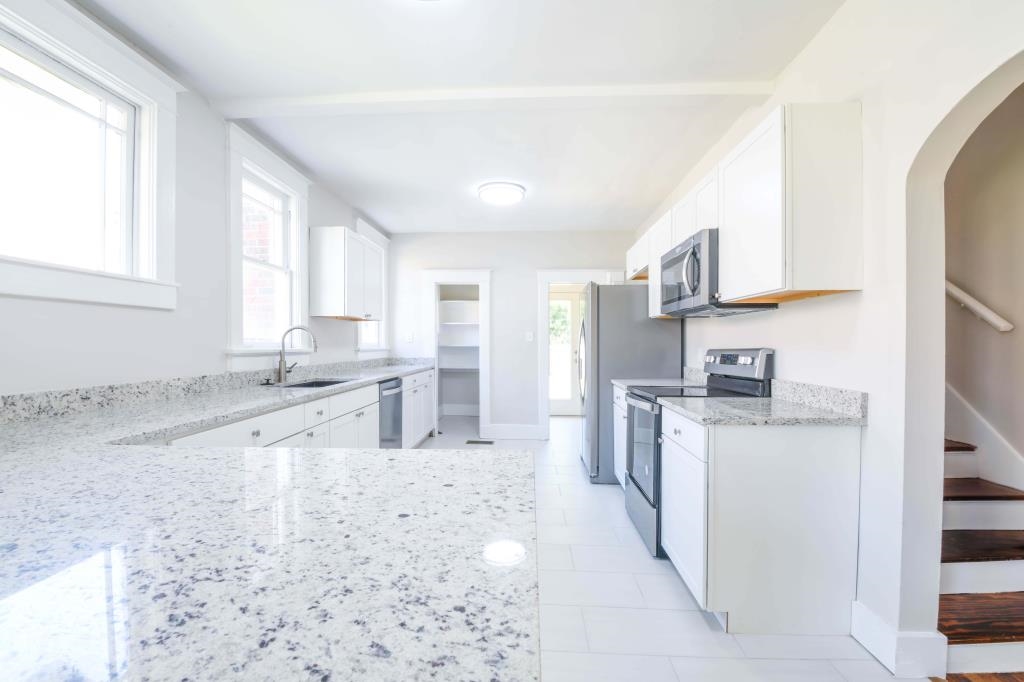 Kitchen with white cabinetry, stainless steel appliances, light stone counters, and plenty of natural light