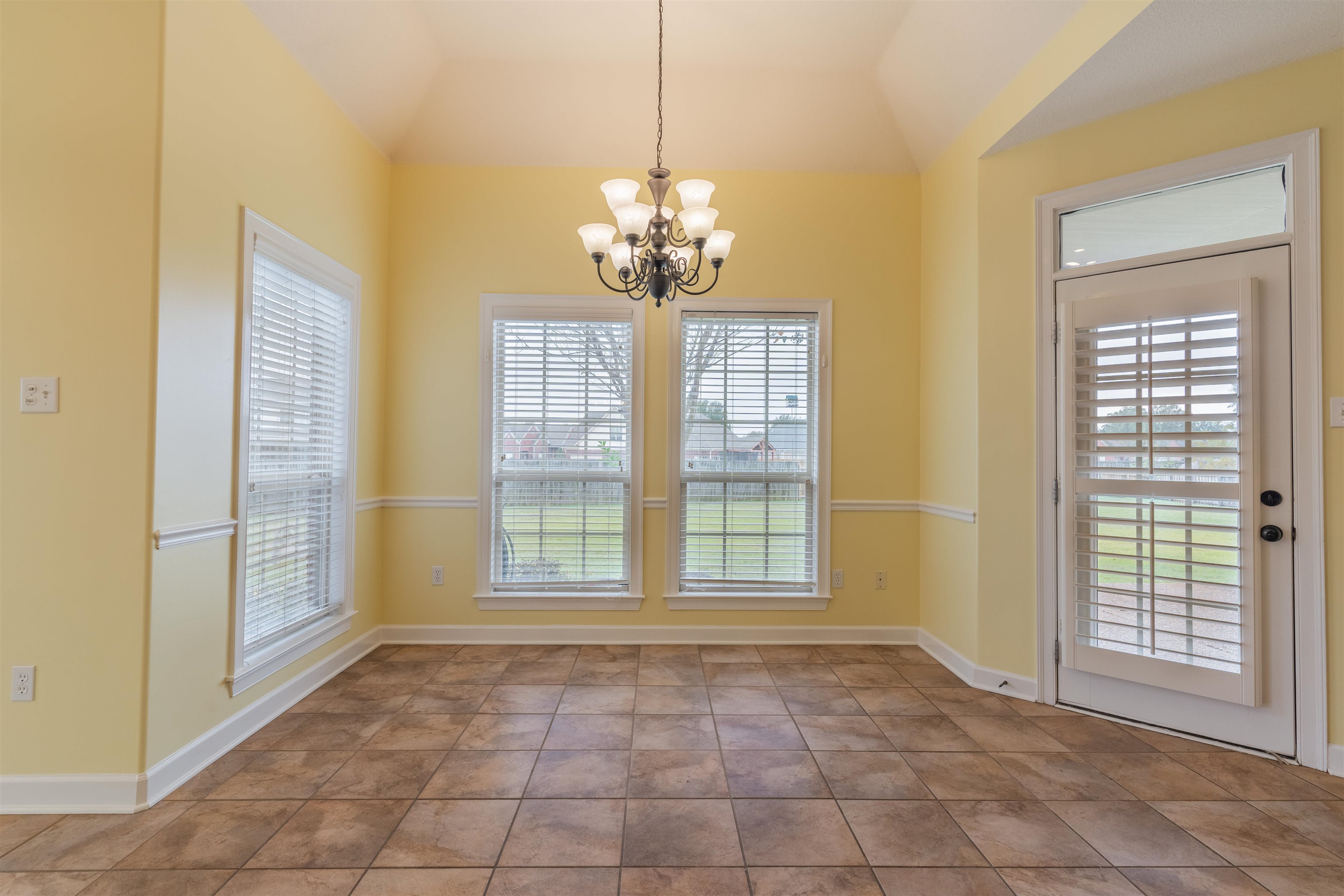 Unfurnished dining area featuring tile patterned flooring, a chandelier, and vaulted ceiling