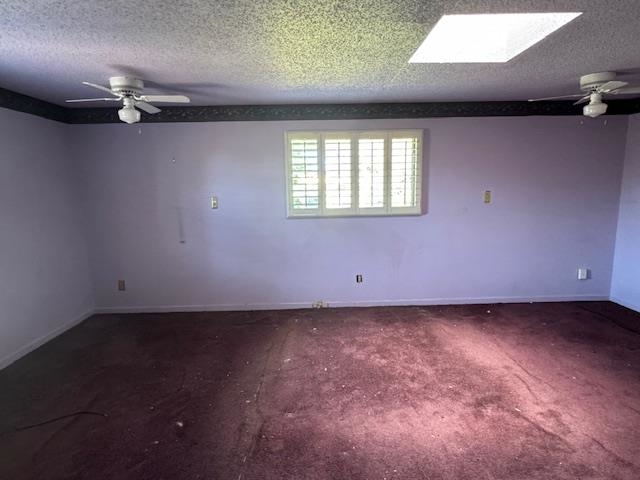 Empty room with a textured ceiling, a skylight, and ceiling fan