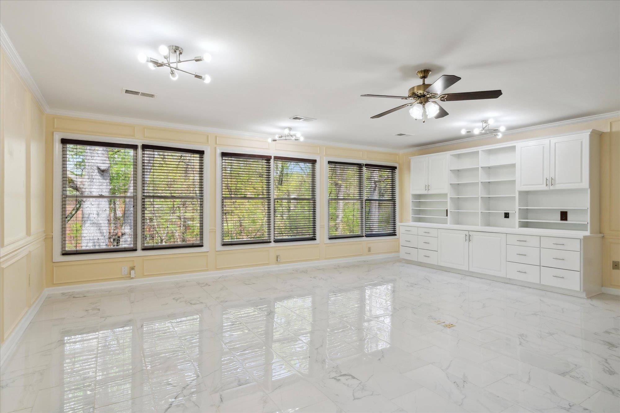 Unfurnished living room featuring built in features, ceiling fan, and crown molding