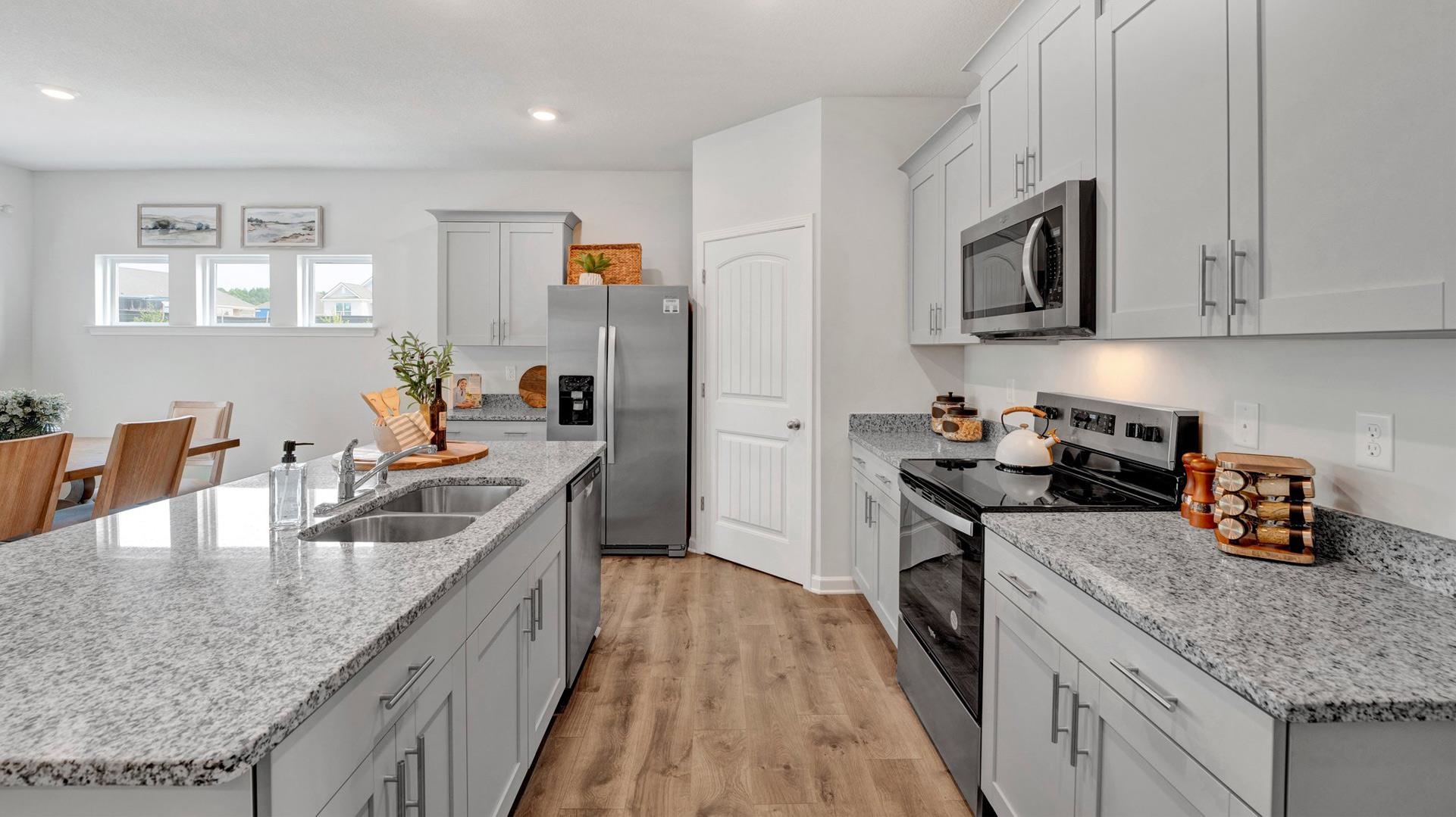 Kitchen with light wood-type flooring, appliances with stainless steel finishes, light stone countertops, sink, and an island with sink