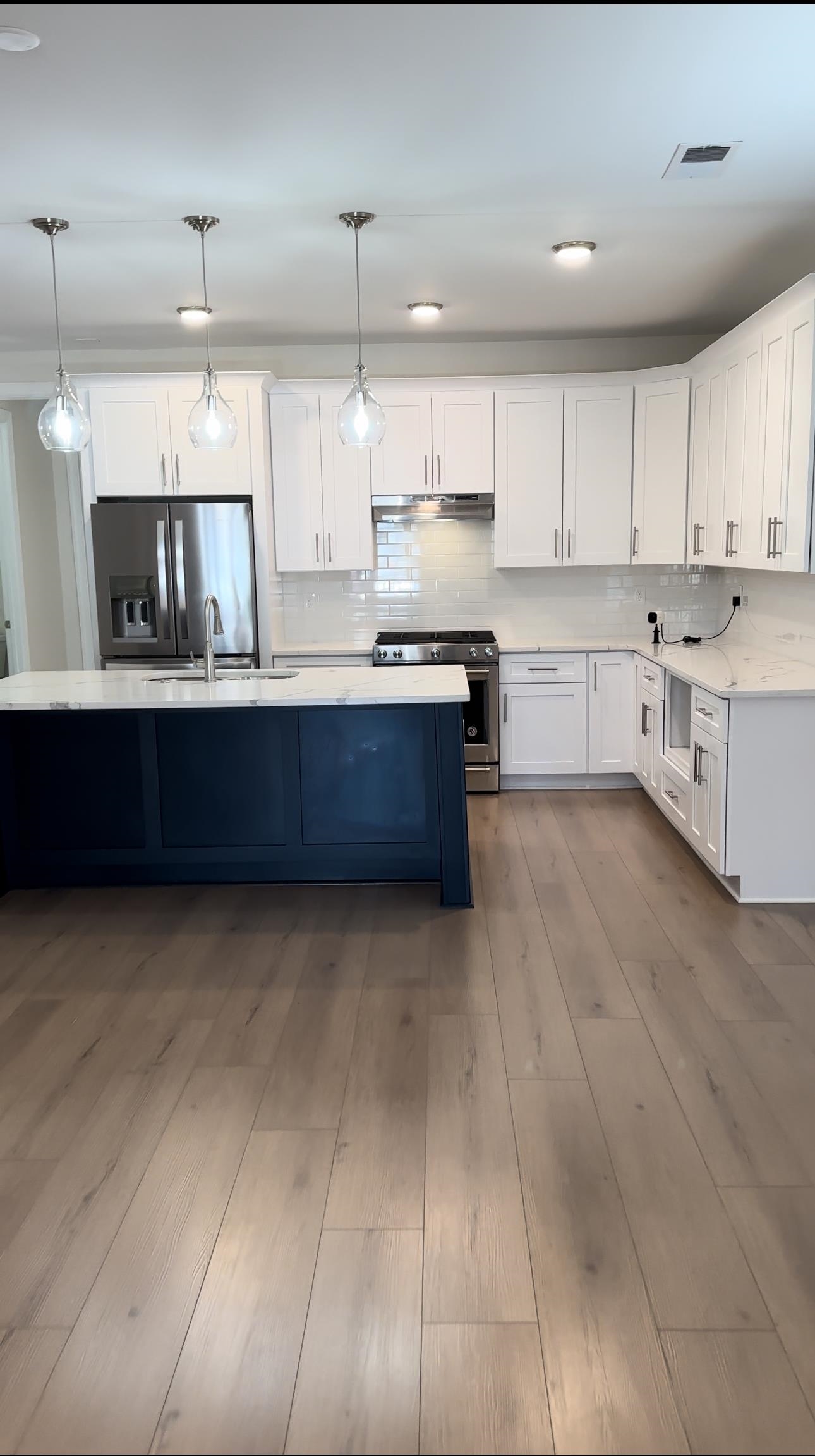 Kitchen featuring white cabinets, appliances with stainless steel finishes, and hanging light fixtures