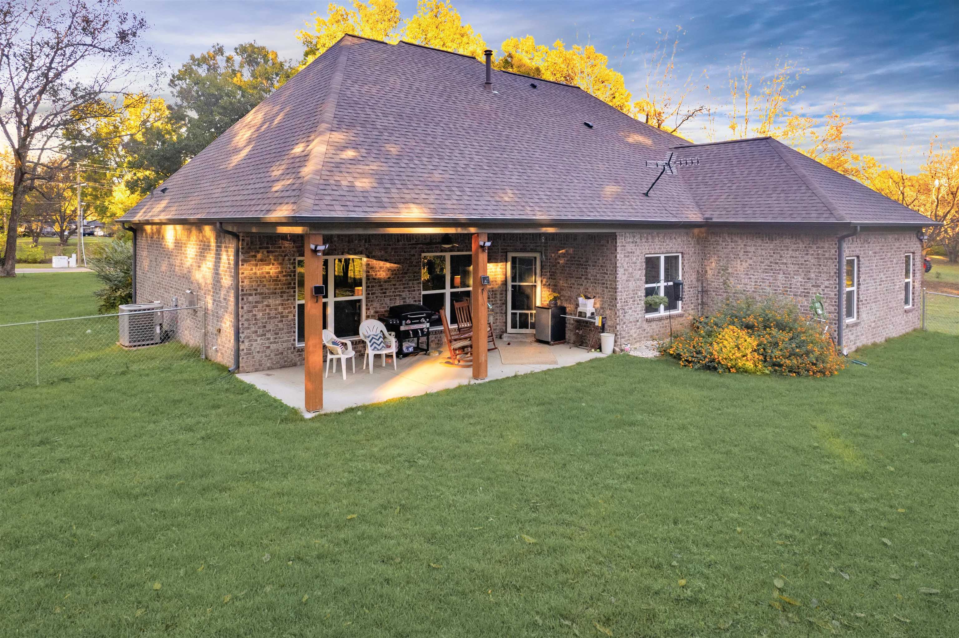 Back house at dusk with central AC unit, a lawn, and a patio