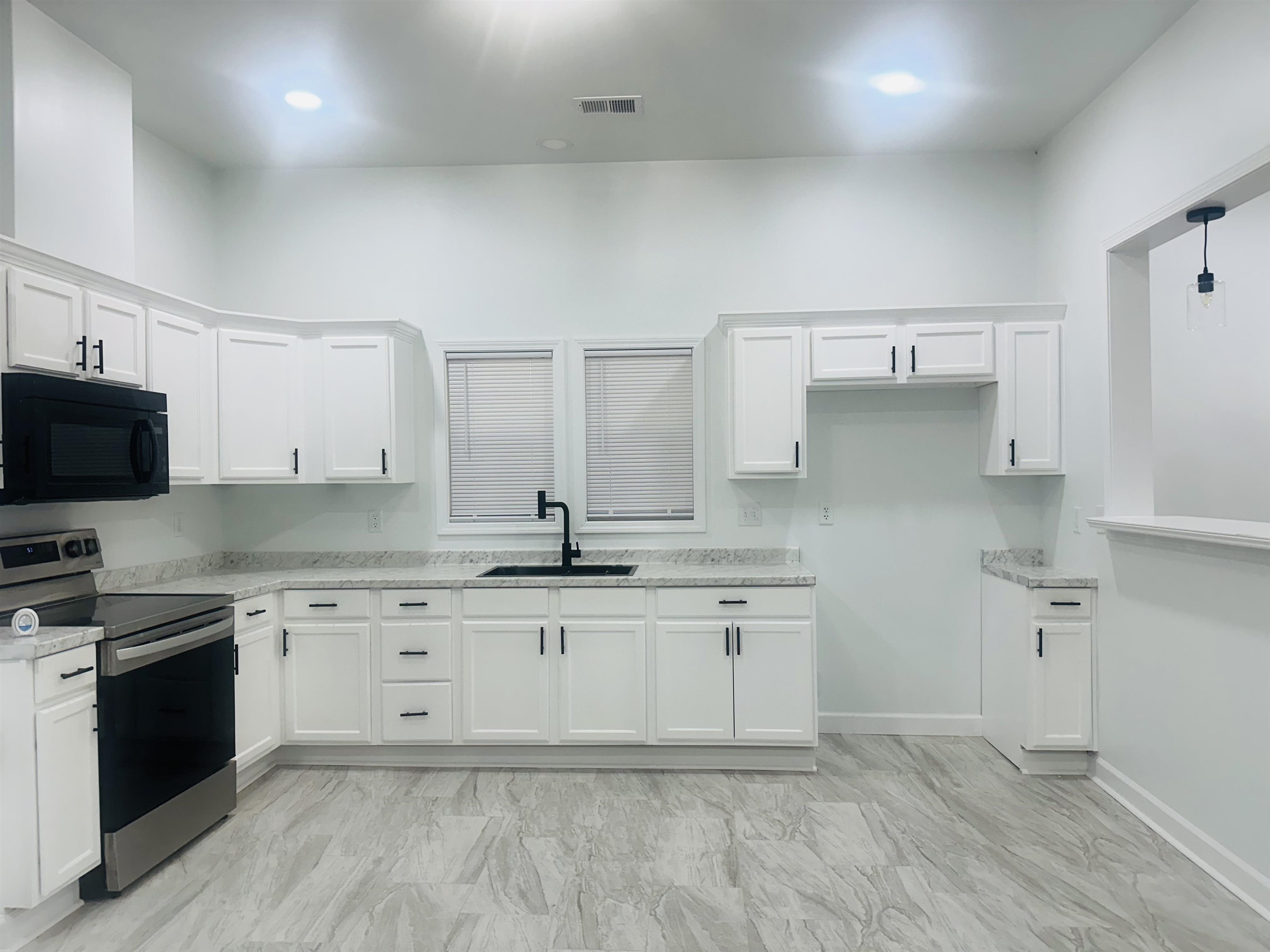 Kitchen with stainless steel electric range, light stone counters, sink, white cabinetry, and decorative light fixtures