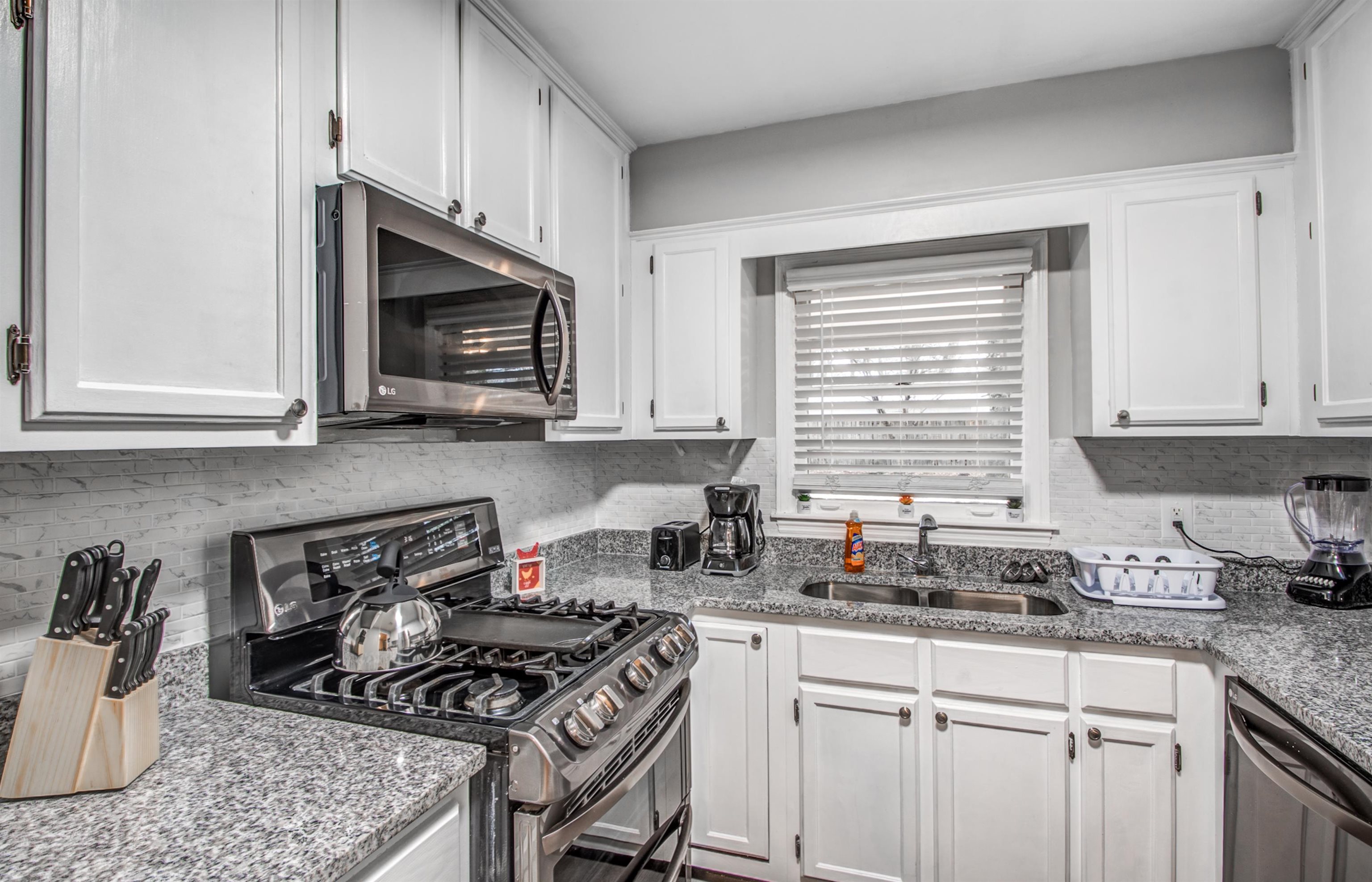 Kitchen featuring white cabinets, sink, light stone counters, and appliances with stainless steel finishes