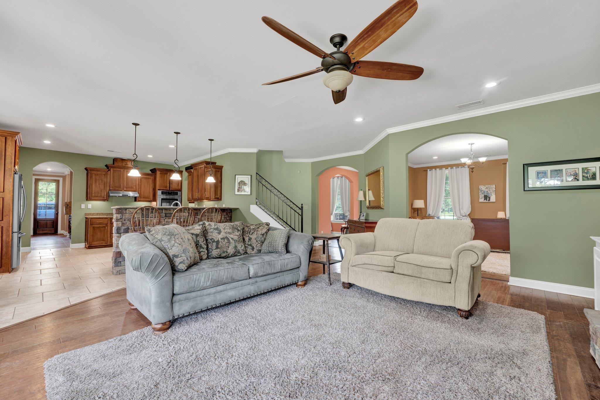 Living room with hardwood / wood-style flooring, ceiling fan with notable chandelier, and crown molding