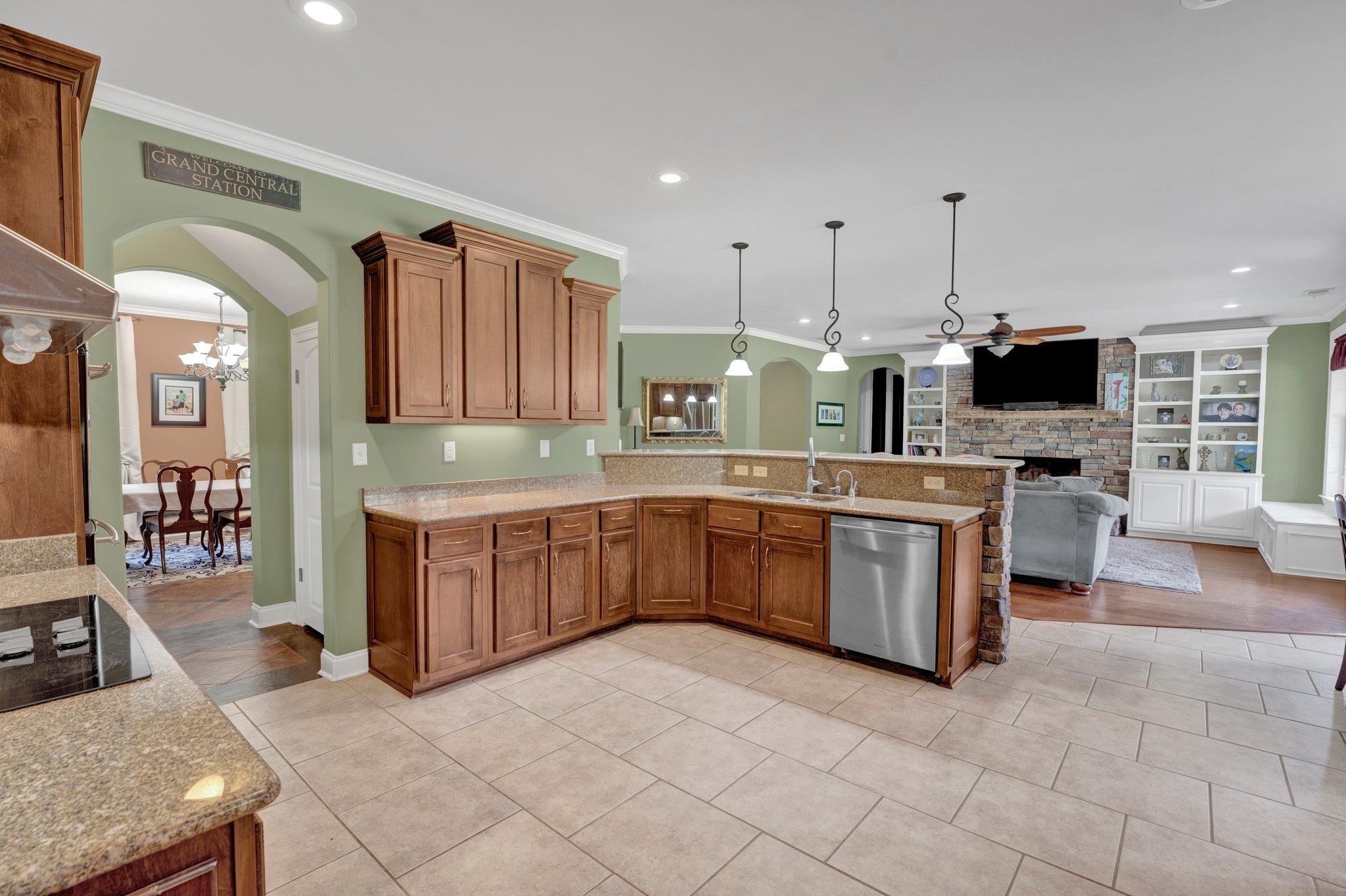 Kitchen with ceiling fan with notable chandelier, stainless steel dishwasher, crown molding, a fireplace, and decorative light fixtures