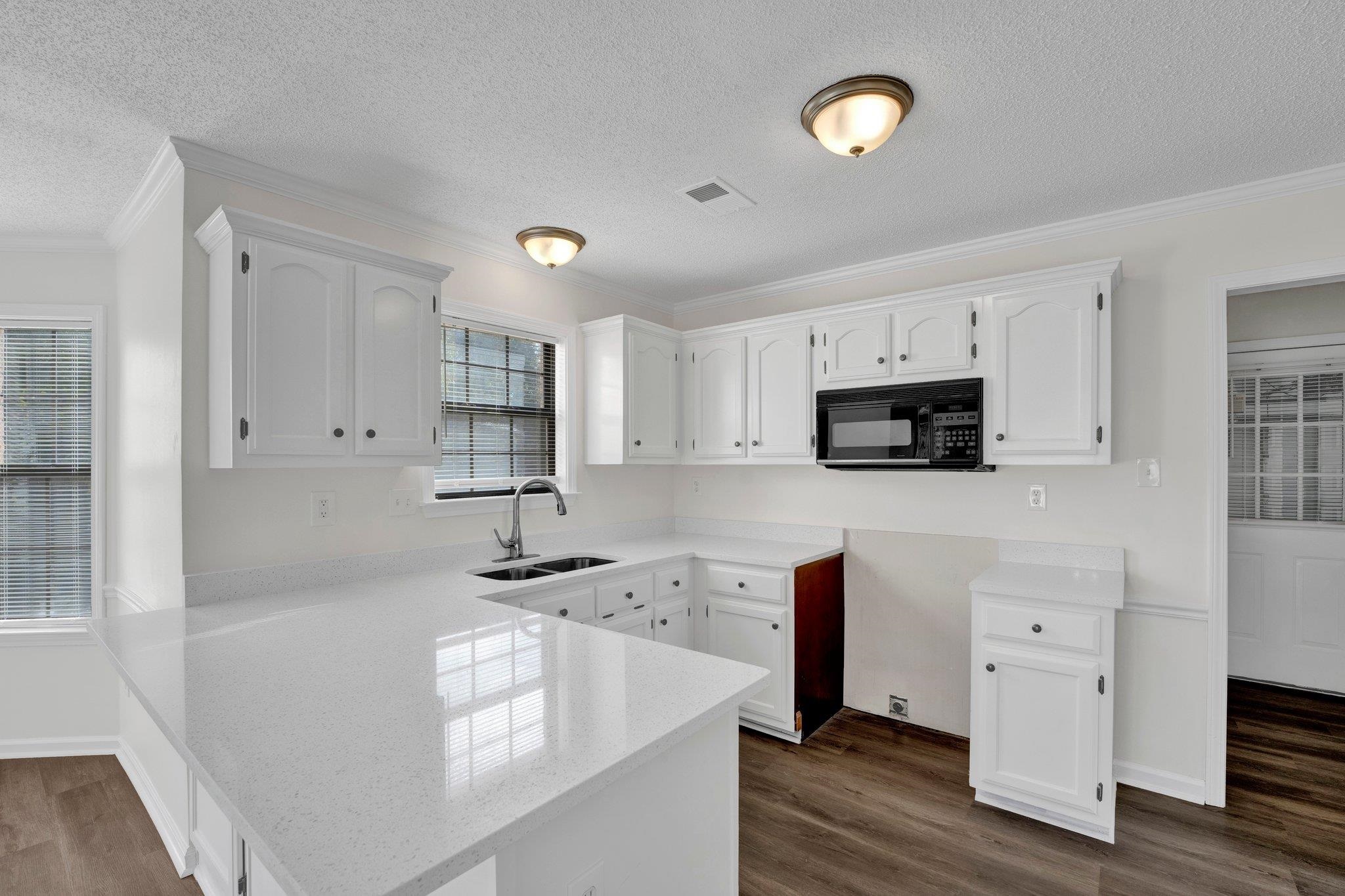 Kitchen with white cabinetry, kitchen peninsula, dark hardwood / wood-style flooring, and sink