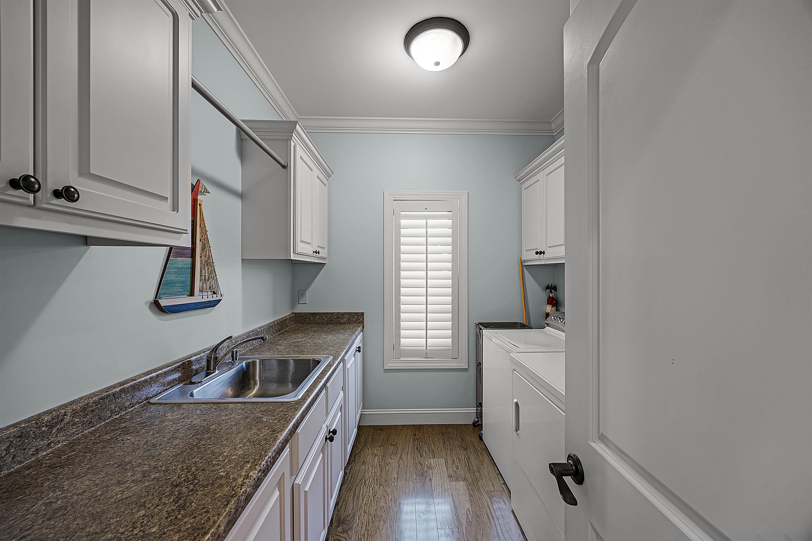 Washroom featuring wood-type flooring, cabinets, sink, crown molding, and independent washer and dryer