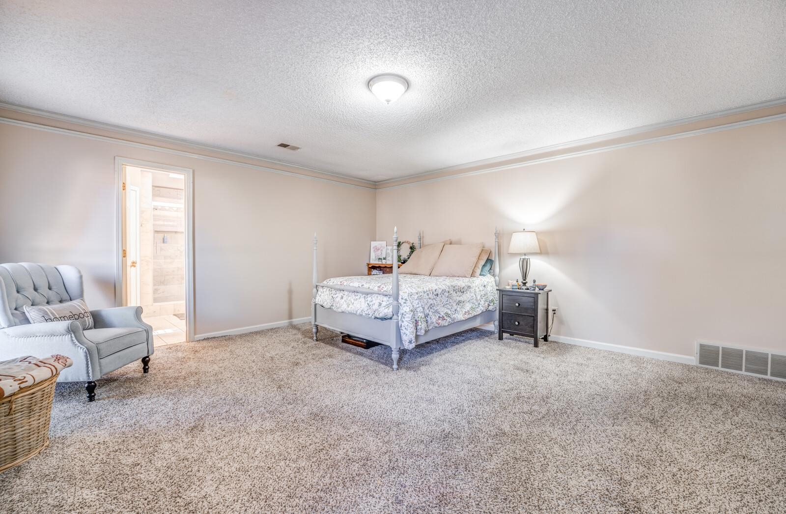 Carpeted bedroom featuring a textured ceiling, connected bathroom, and crown molding