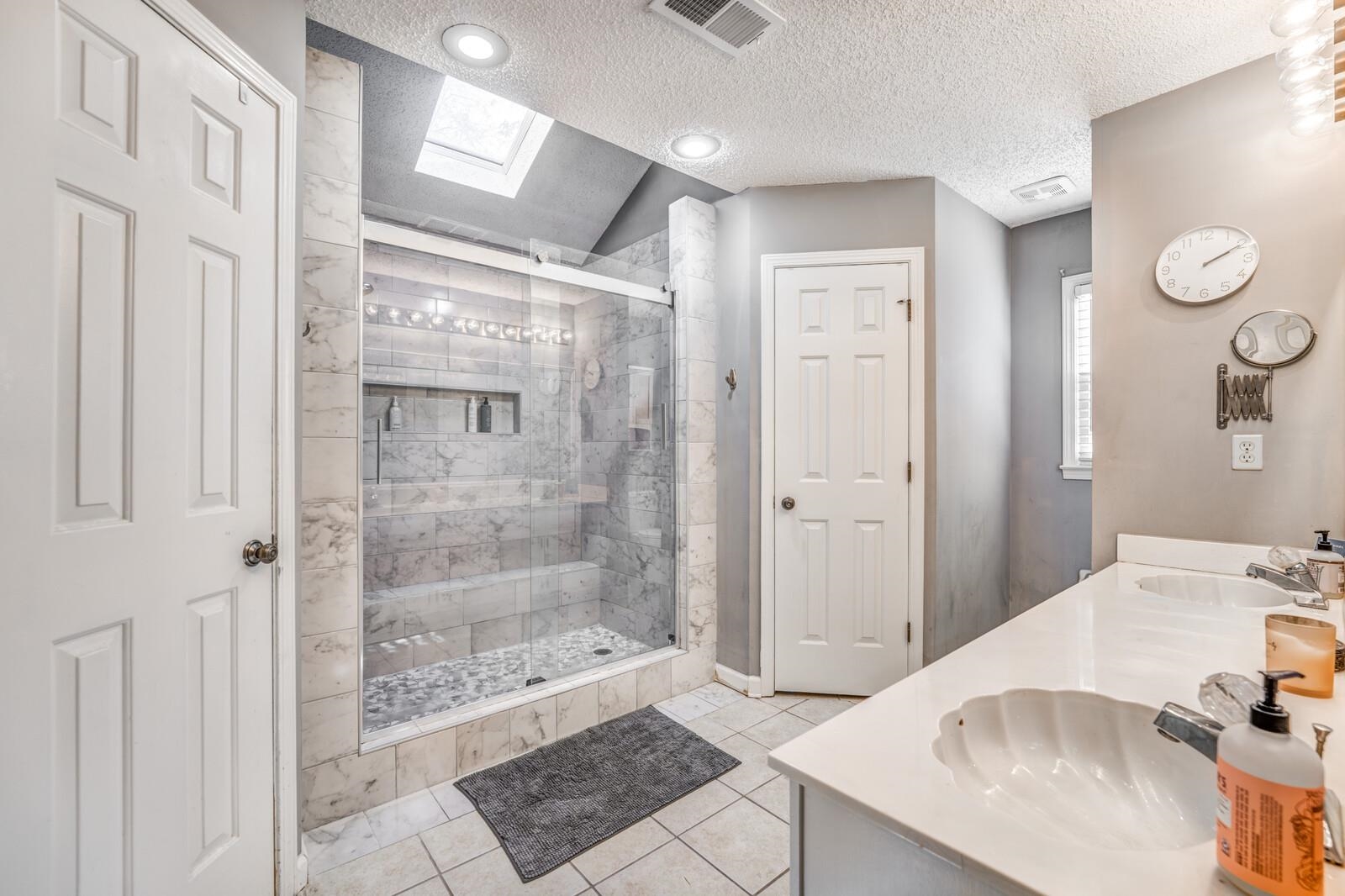 Bathroom with vaulted ceiling with skylight, a textured ceiling, vanity, tile patterned flooring, and a shower with shower door