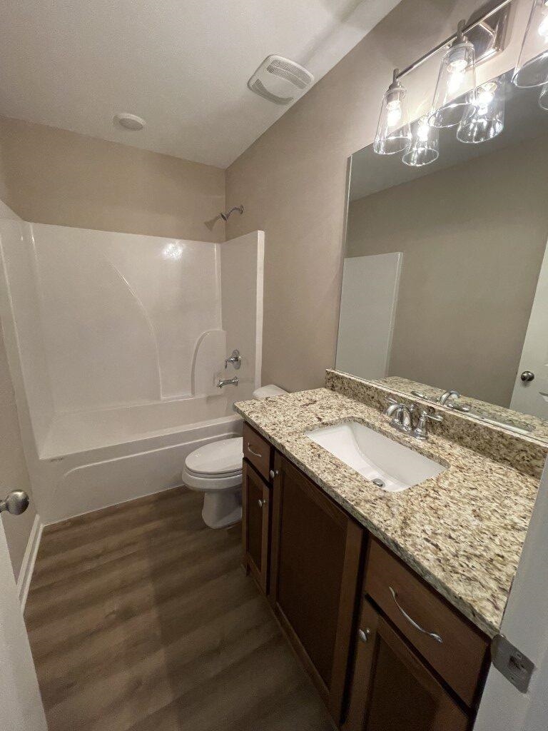 Full bathroom featuring hardwood / wood-style floors, vanity, toilet, and shower / tub combination