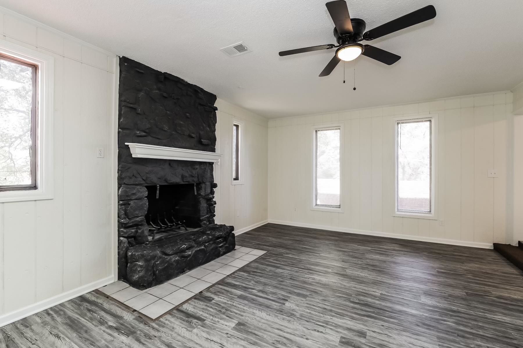 Unfurnished living room with hardwood / wood-style floors, ceiling fan, plenty of natural light, and a stone fireplace