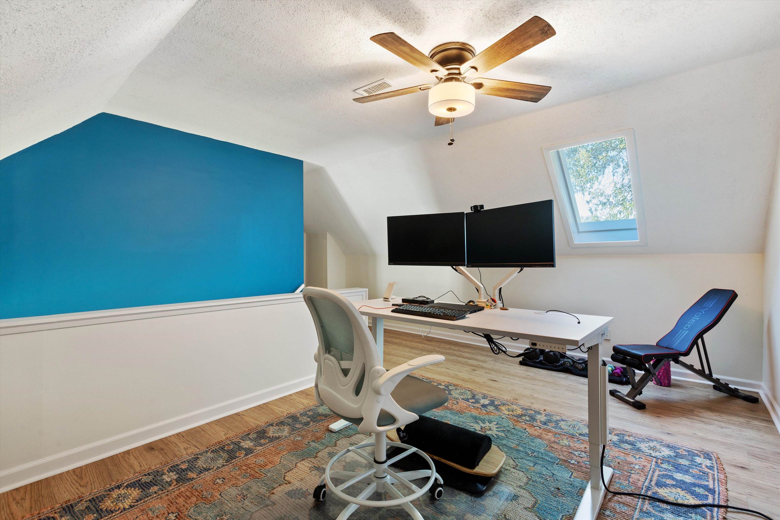 Third floor office with a textured ceiling, hardwood / wood-style flooring, lofted ceiling with skylight, and ceiling fan