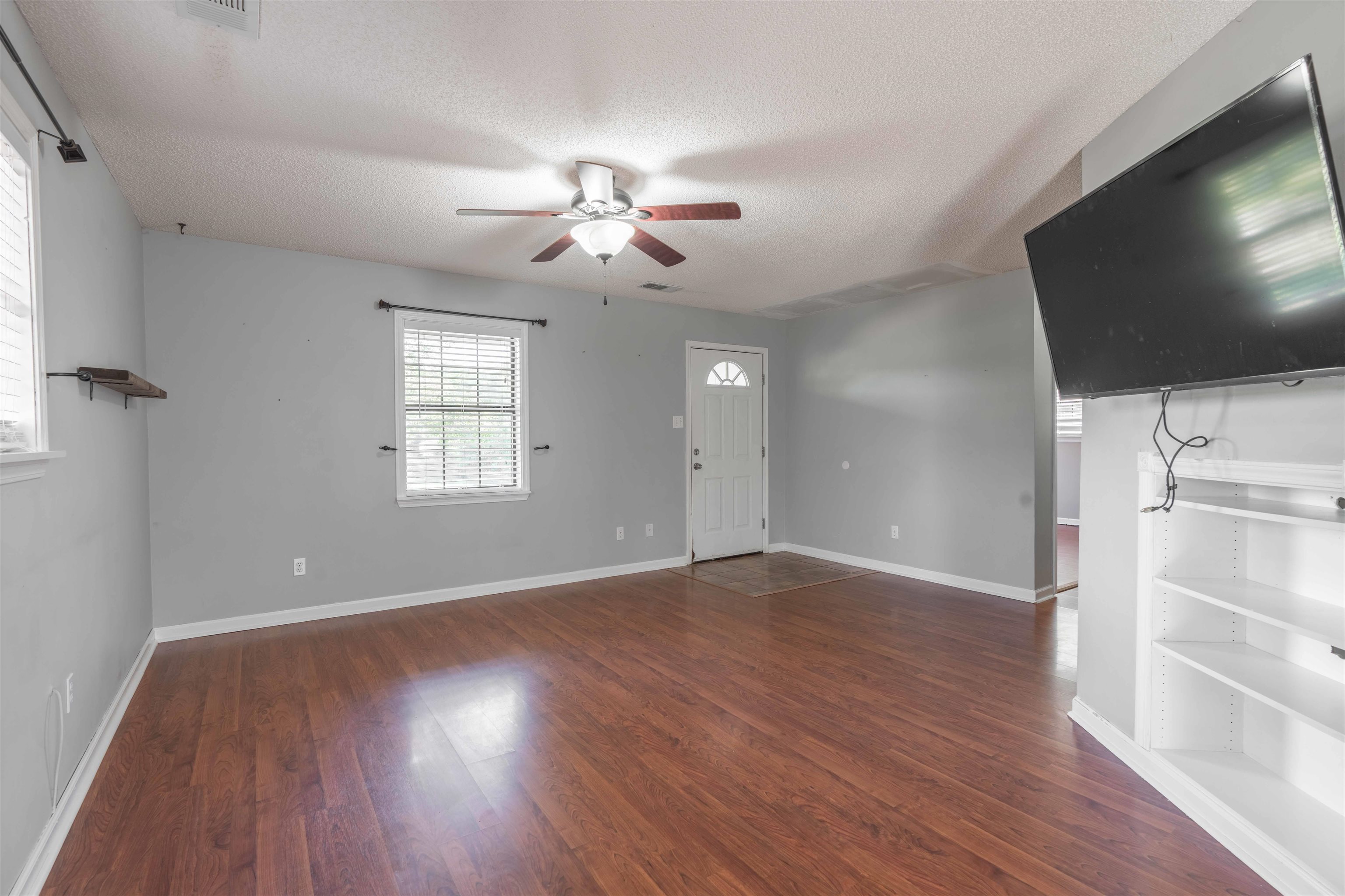 Unfurnished living room featuring ceiling fan, dark wood-type flooring, and a textured ceiling